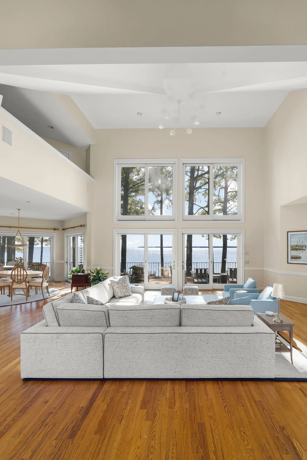 Spacious waterfront living room designed by AWH Interiors in Williamsburg, featuring soft blue accents, layered neutrals, and natural wood tones that echo the coastal surroundings.