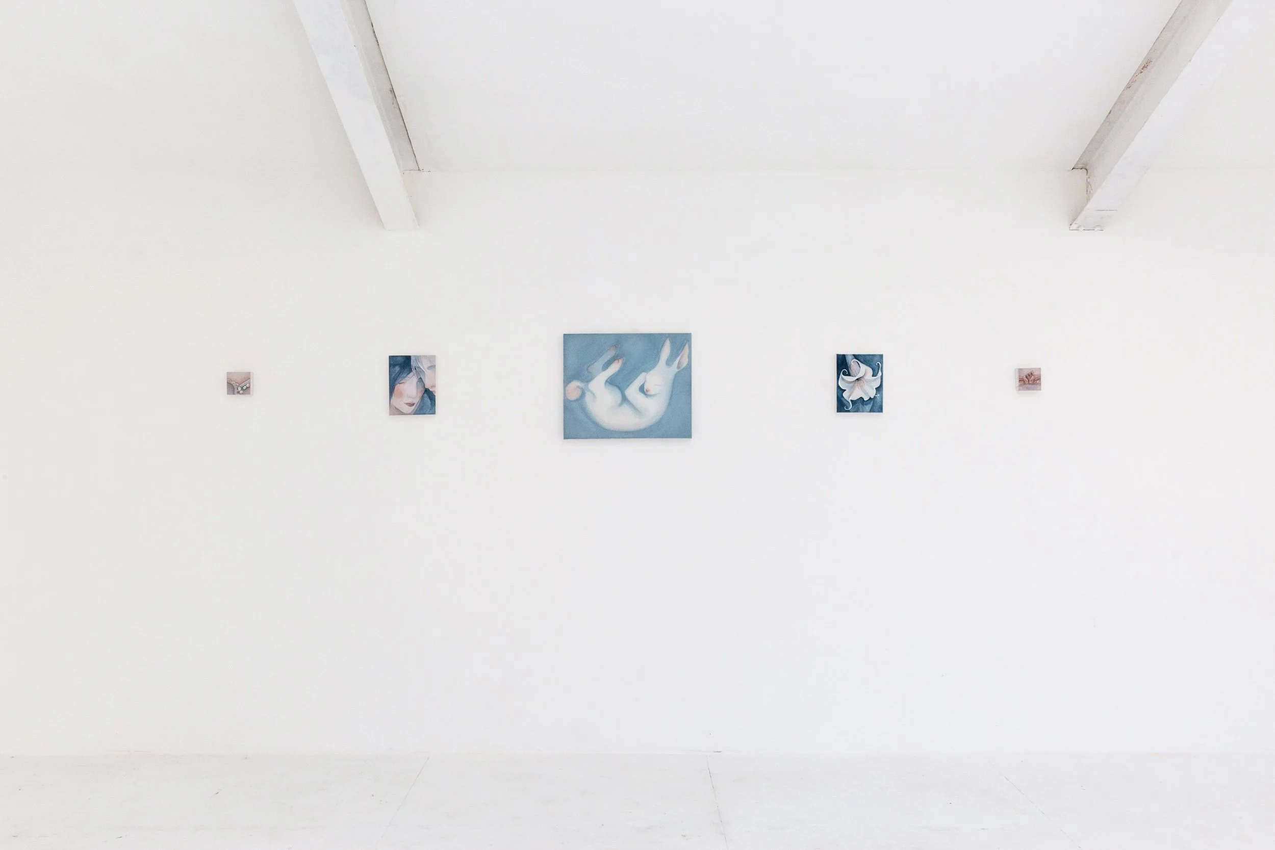 White gallery wall with five artworks, including one large central piece depicting abstract white figures on a blue background, and four smaller art pieces flanking it.