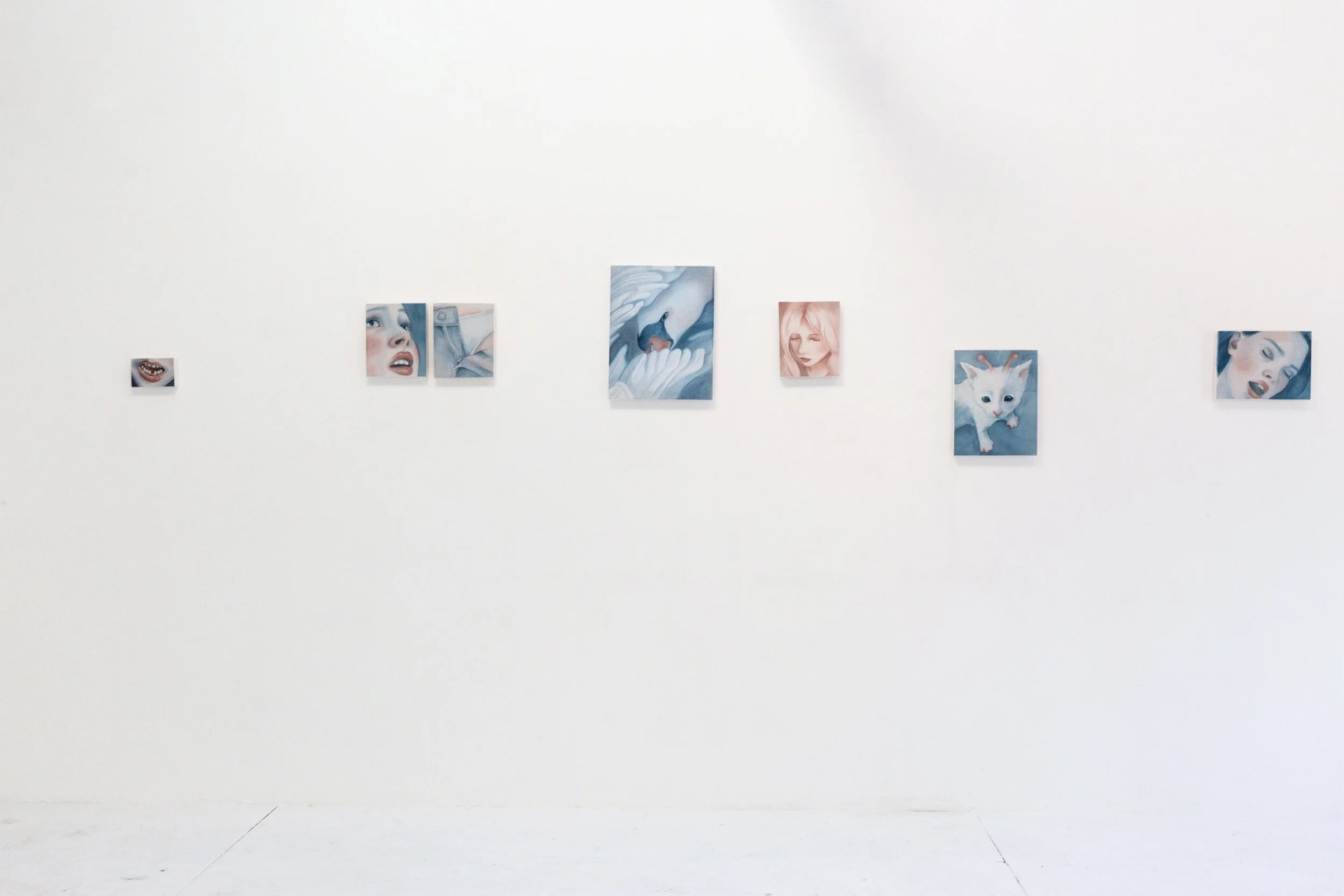 A white wall with a series of seven small, rectangular art pieces arranged in a horizontal line.