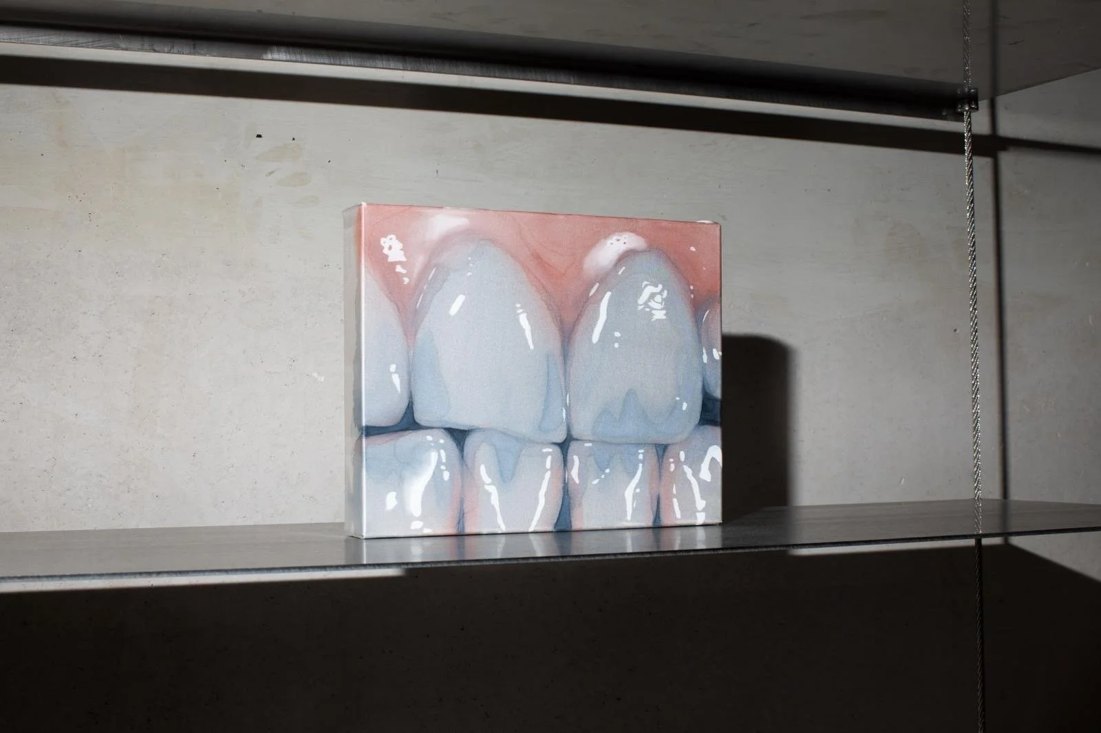 Painted artwork of three sets of teeth with gums, in a realistic style, resting on a shelf.