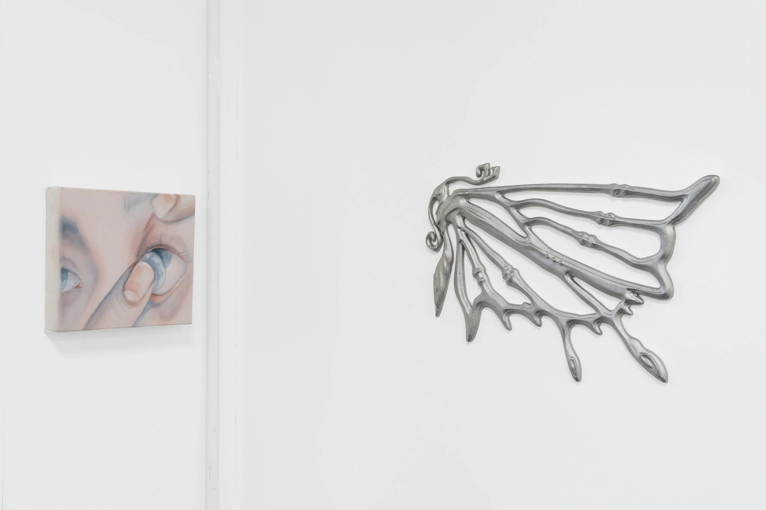 Artwork with a small painting of a hand holding a lit cigarette and a metallic butterfly sculpture on a white wall.