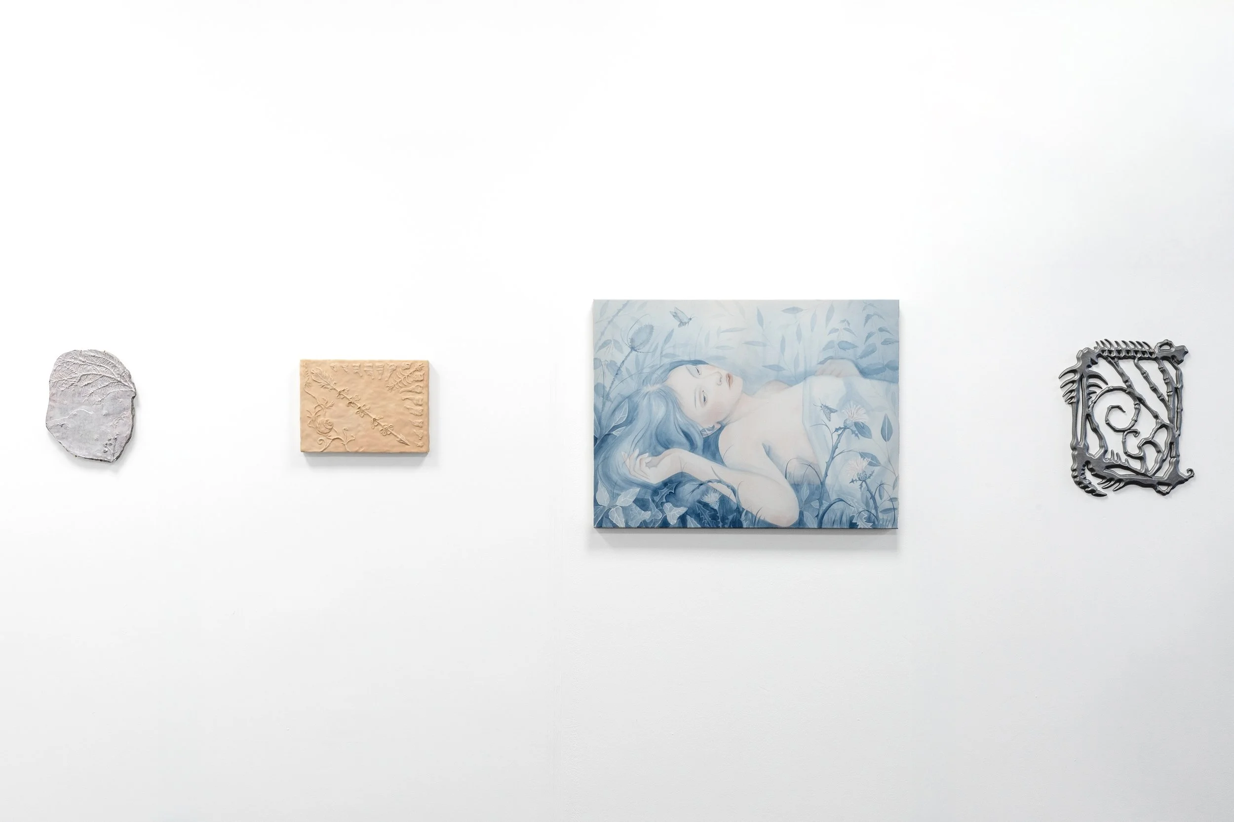 A white gallery wall with five art pieces: a textured gray stone, a small beige relief with a plant design, a large portrait of a female figure with blue hair lying among plants and butterflies, a dark metal abstract sculpture, and a black decorative