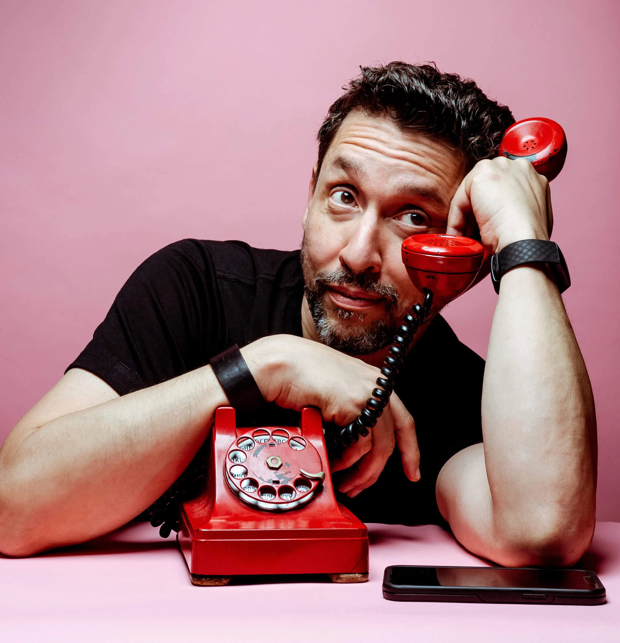 Rick Ferrari sitting with a red rotary phone and cell phone with a pink background