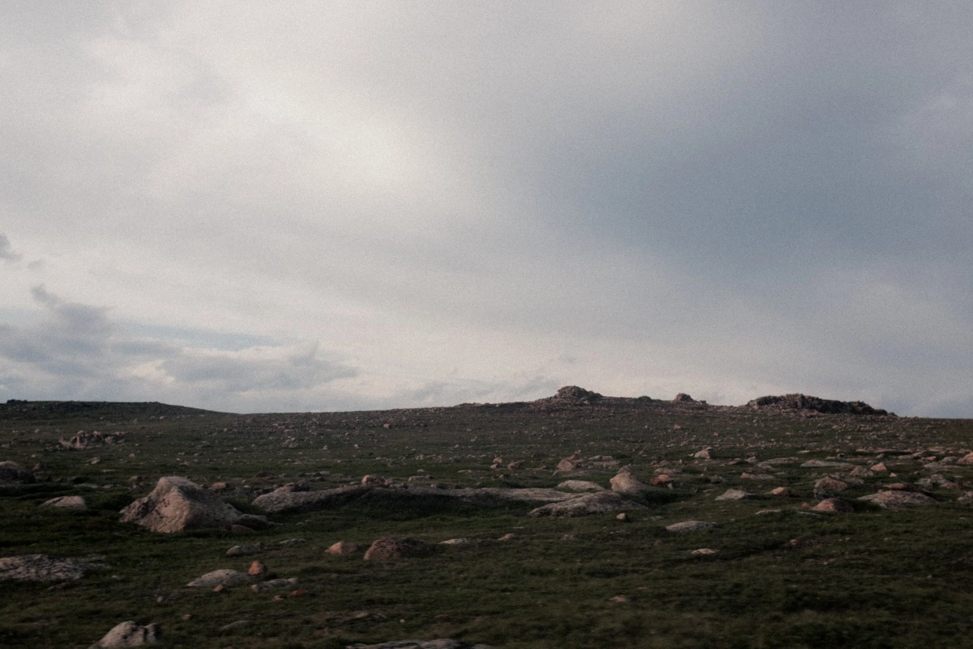 A vast open landscape with grassy terrain and scattered rocks under a cloudy sky.