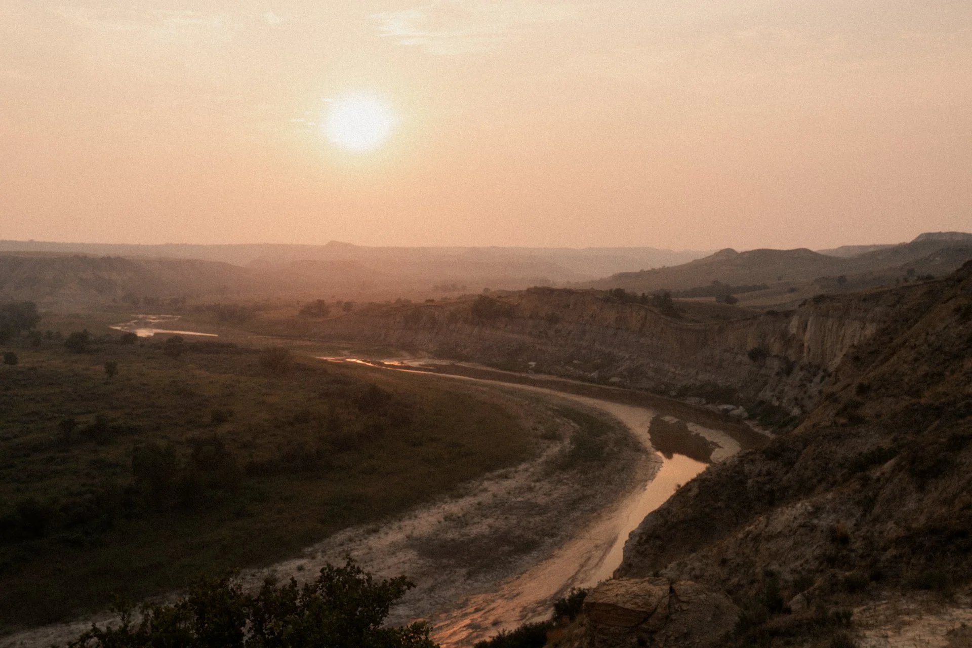Sun setting over a winding river through a hilly landscape.