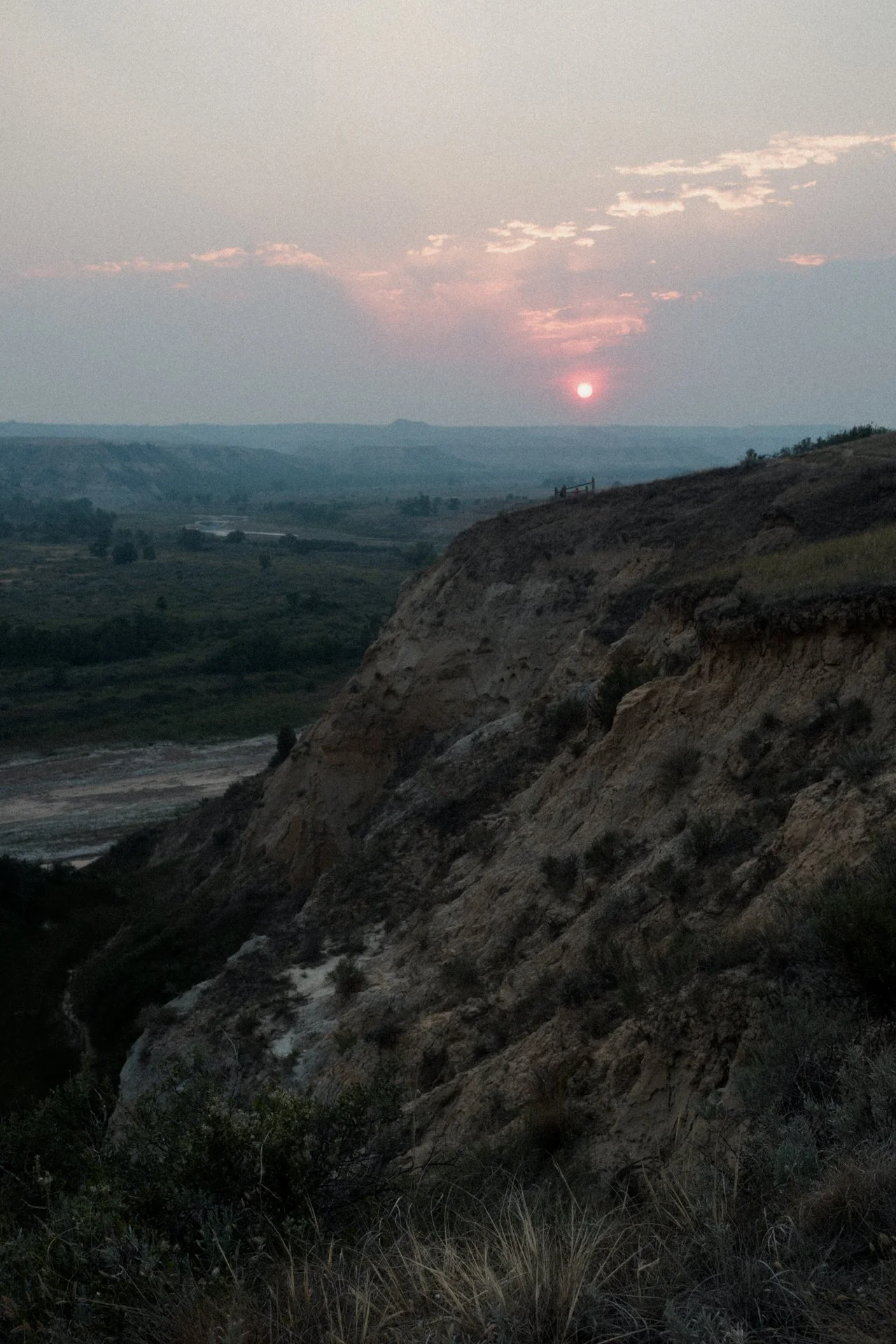 Sunset over a mountainous landscape with rocky cliffs, green vegetation, and a river in the valley below.