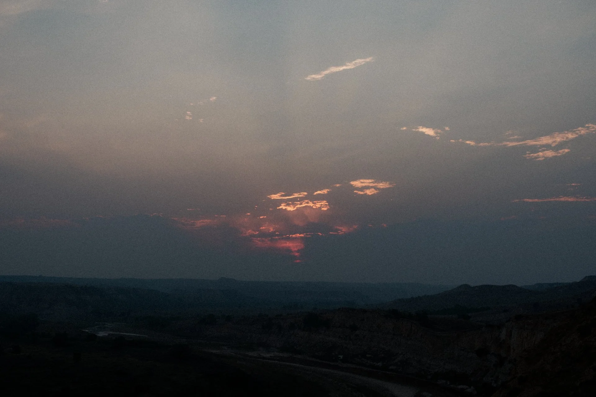 Sunset over a mountainous landscape with a dark sky and scattered clouds.