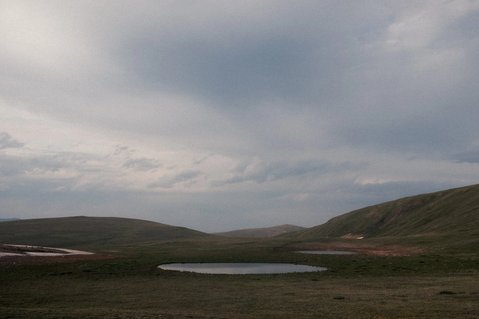 A landscape scene with rolling green hills, small ponds, and a cloudy sky.