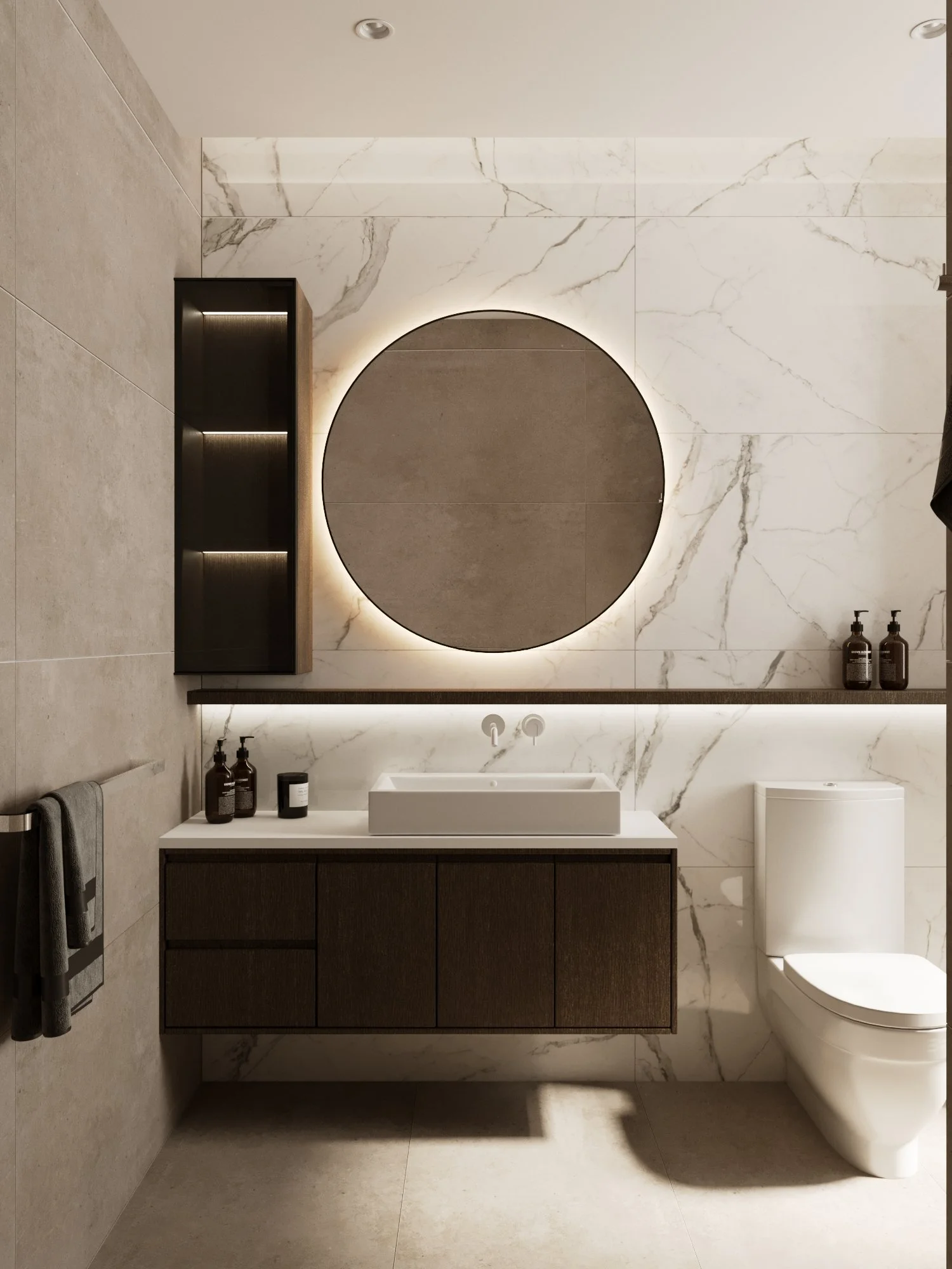 Modern bathroom with a large round backlit mirror, white sink on a dark wooden cabinet, and a toilet. The wall behind features large marble tiles, and a wooden shelf with black bottles. A towel hangs on the left, and recessed ceiling lights.