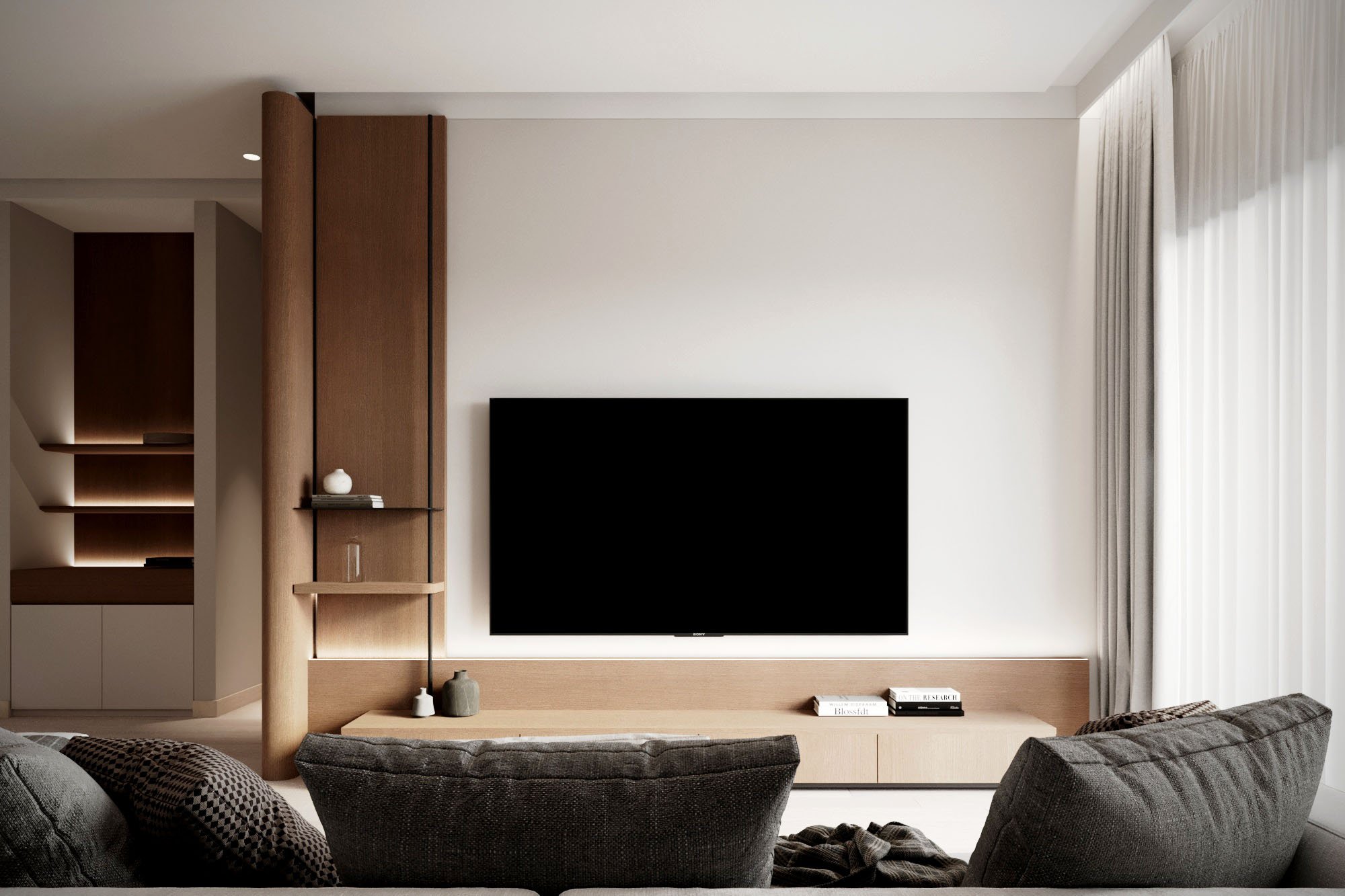 Modern living room with a large flat-screen TV on the wall, wooden shelving, and dark upholstered sofa.