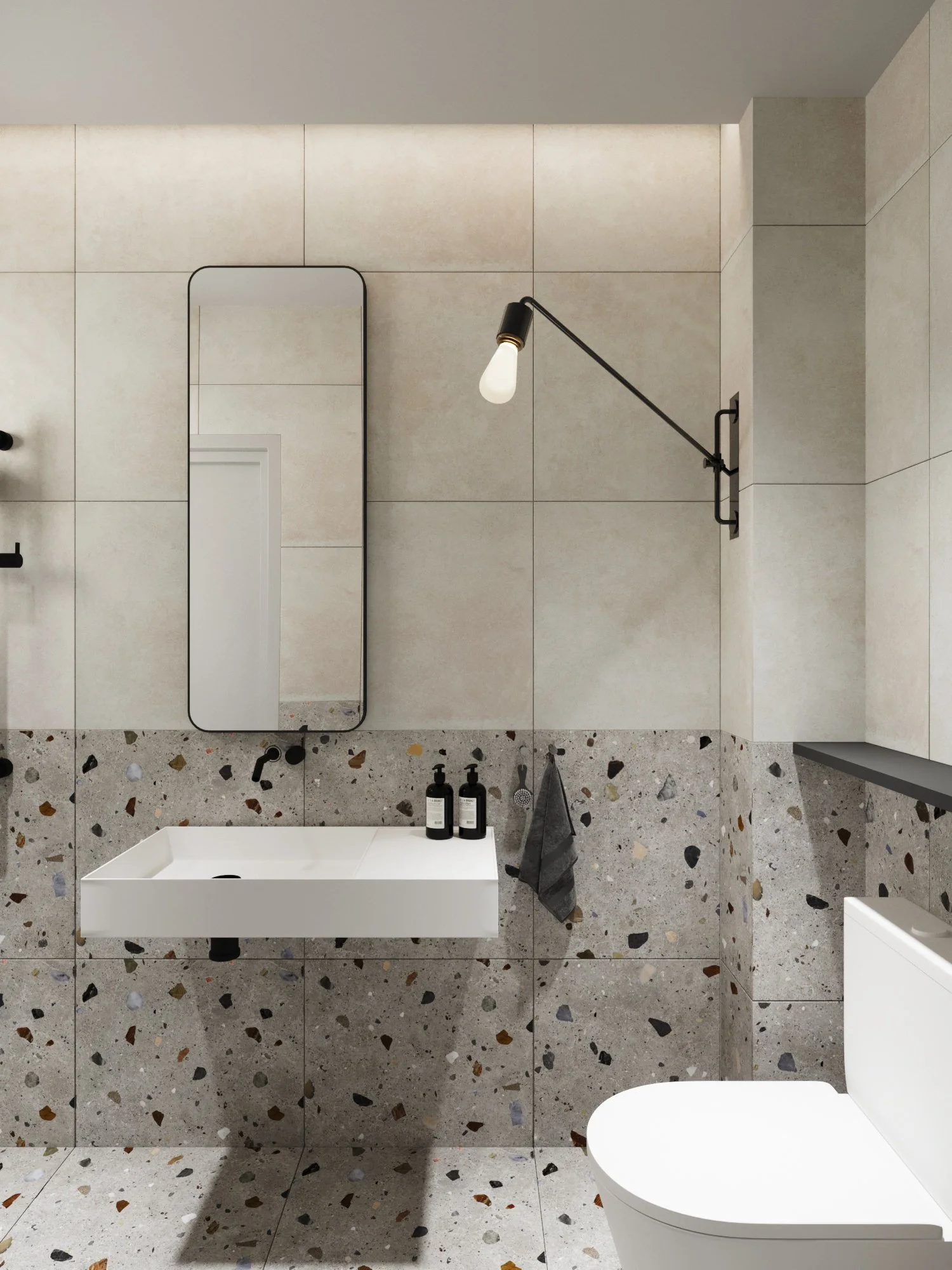Modern bathroom with beige tiled walls, terrazzo floor, wall-mounted sink, oval mirror, black wall-mounted light fixture, black soap dispensers, dark gray hand towel, and white toilet.