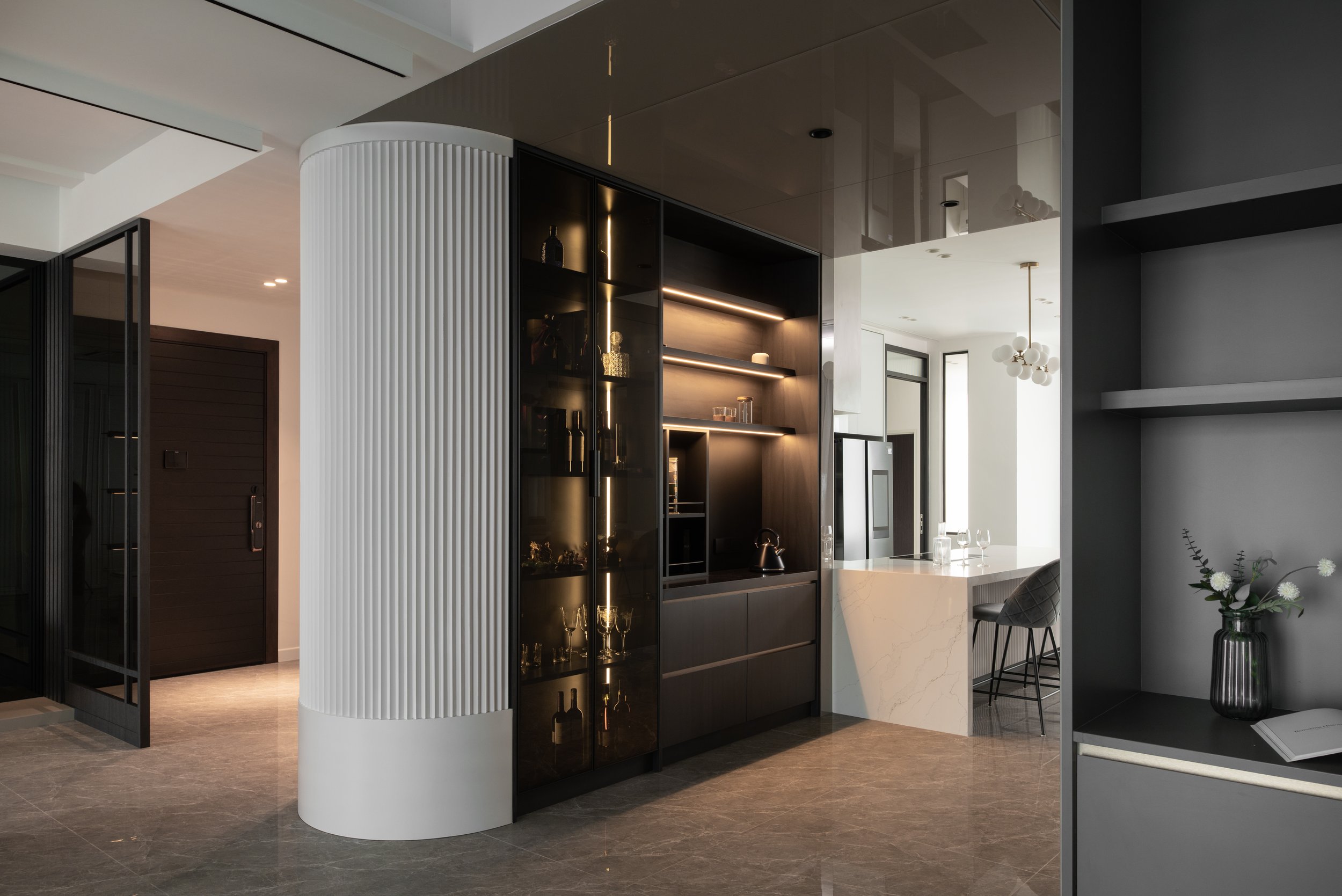 Modern kitchen with black cabinetry, a built-in oven, illuminated shelves, and a marble kitchen island with glassware.