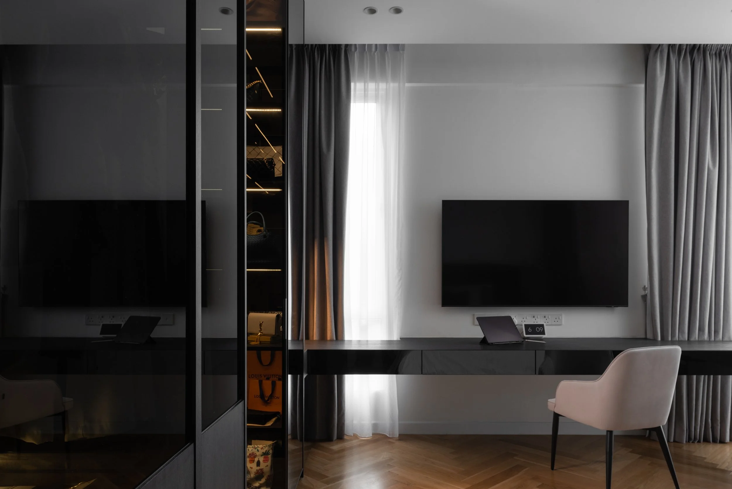 Modern hotel room with a black desk, pink chair, wall-mounted TV, and large curtains near a window with natural light.