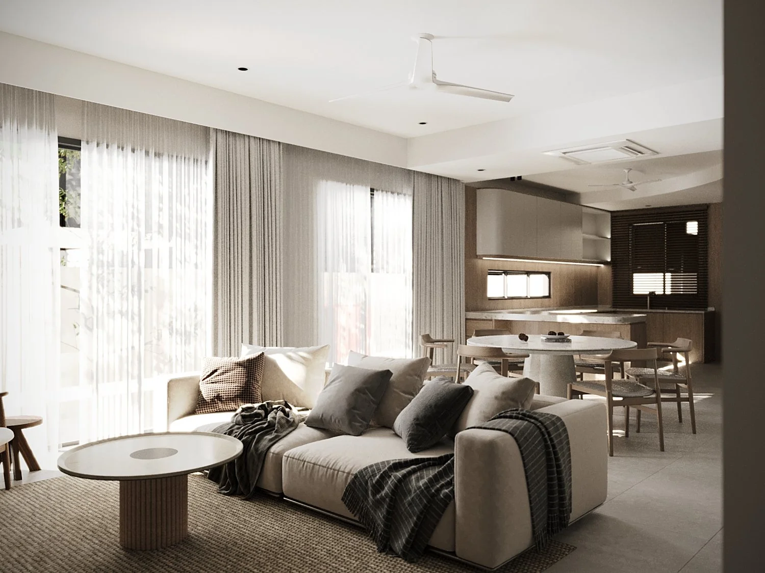 Modern living room with a beige sofa, pillows, throw blanket, round coffee table, and large windows with sheer curtains, opening into a kitchen and dining area with a dining table and chairs.