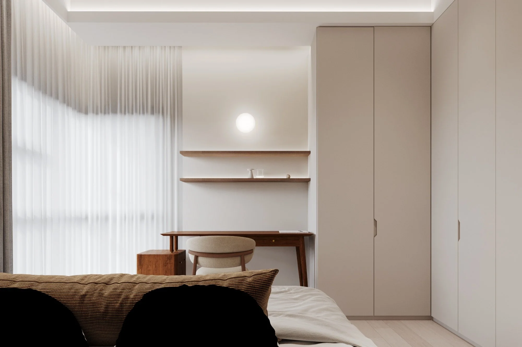 A minimalist bedroom with a beige bed, pillow, and blanket, a wooden desk with a matching chair, white shelving on the wall, and a large wardrobe with beige doors. Sunlight filters through sheer curtains.