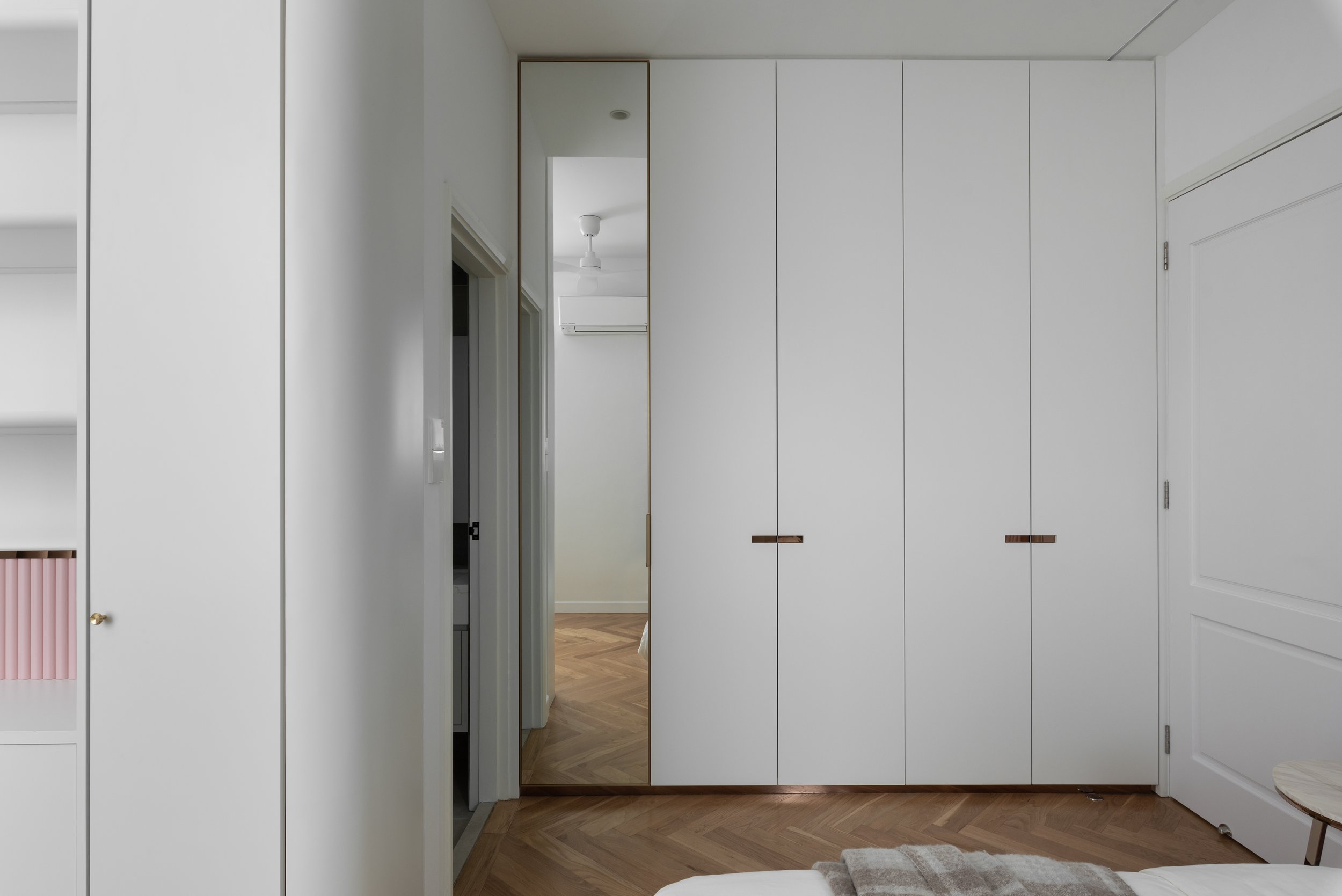 Interior view of a bedroom with a large white wardrobe, a mirror, and wood flooring.