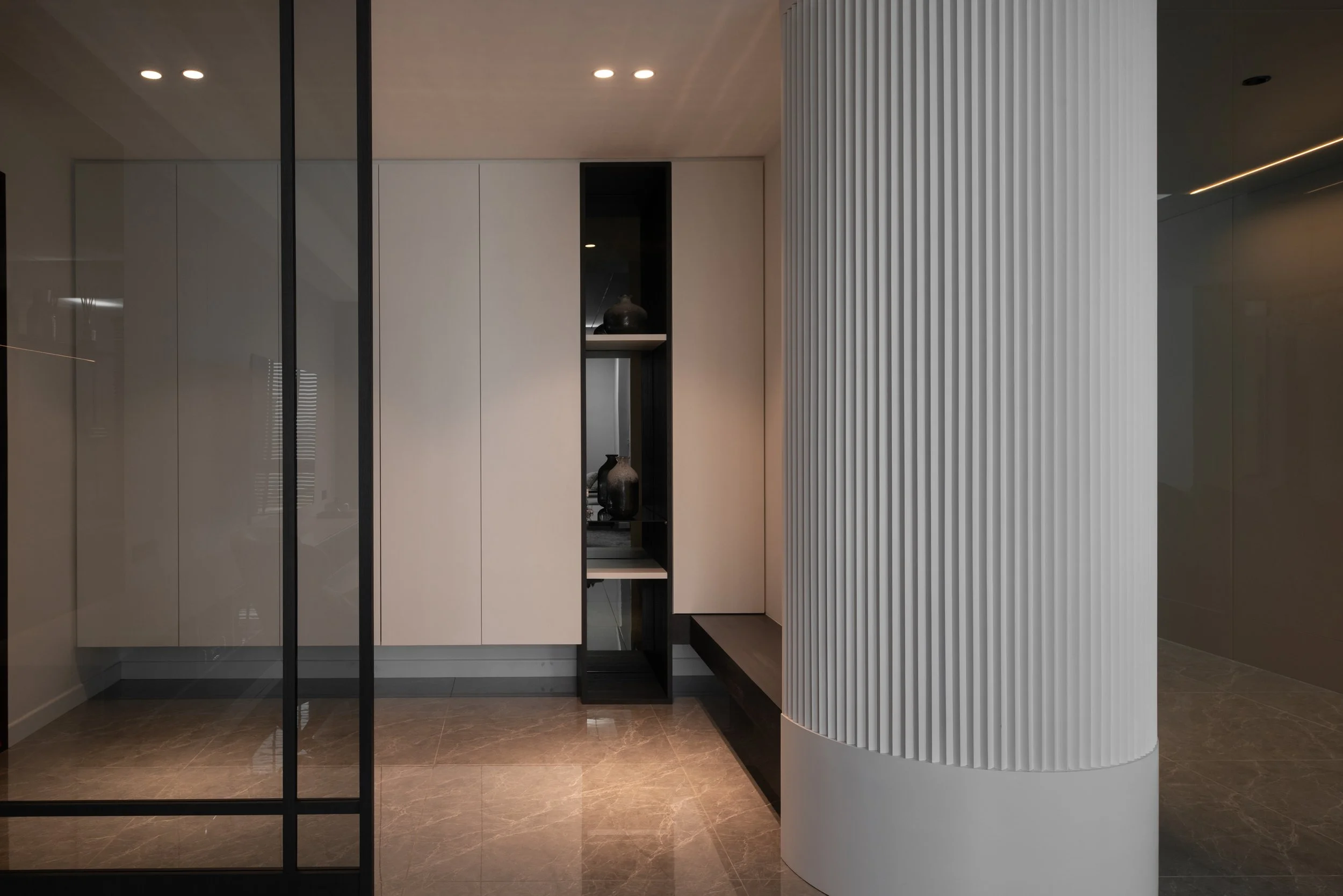 Modern minimalist interior with beige cabinets, black open shelving, decorative vases, and a large rounded white ribbed column.