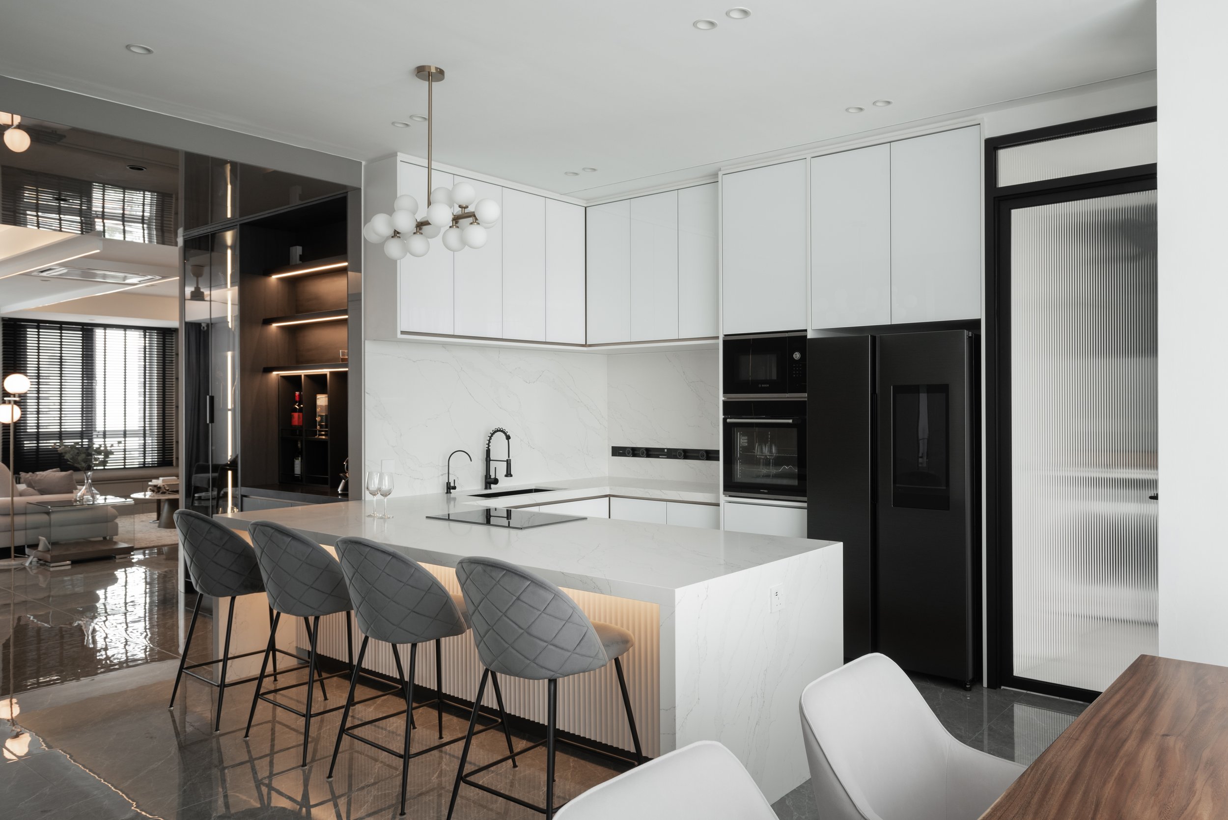 Modern kitchen with white cabinets, black appliances, a marble island, and a dining area with white chairs.