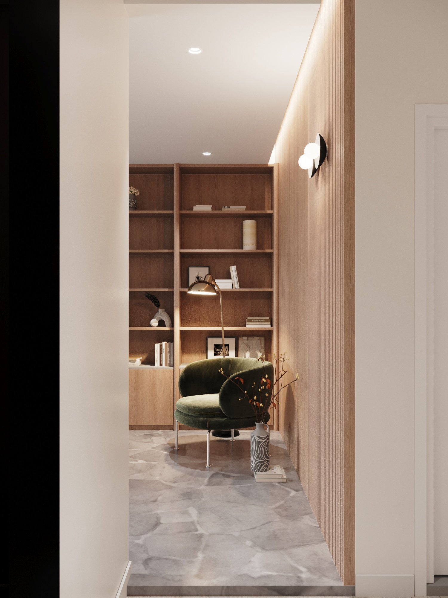 A cozy reading nook with a green velvet chair, a tall floor lamp, a wooden bookshelf filled with books and decorative items, a vase with branches, and a marble floor.