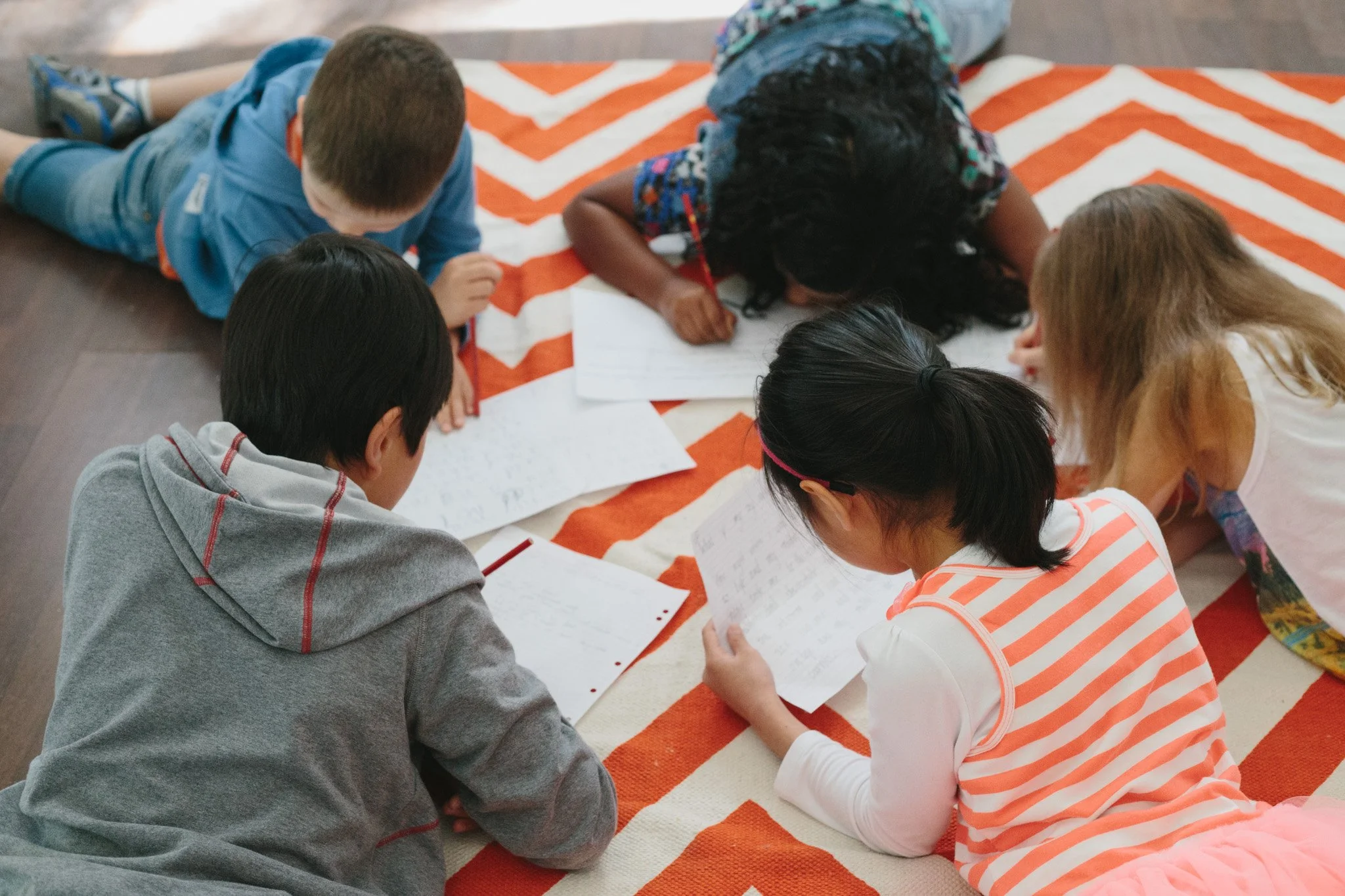 Five kids lying on the floor handwriting their stories as part of a kids' creative writing program in Melbourne.