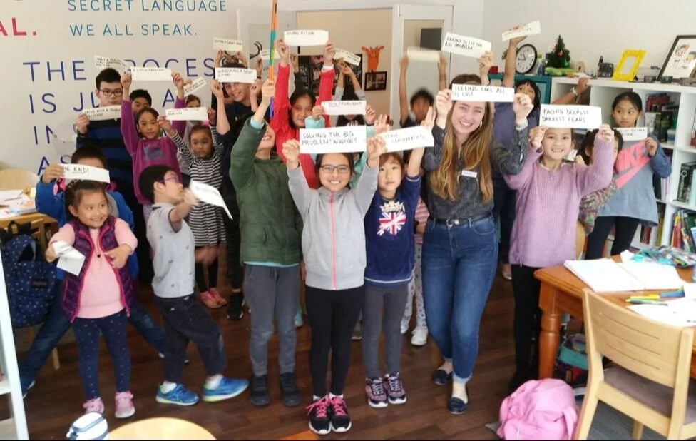 A group of kids excitedly holding up excerpts of their writing from a school holiday creative writing program for kids in Melbourne.
