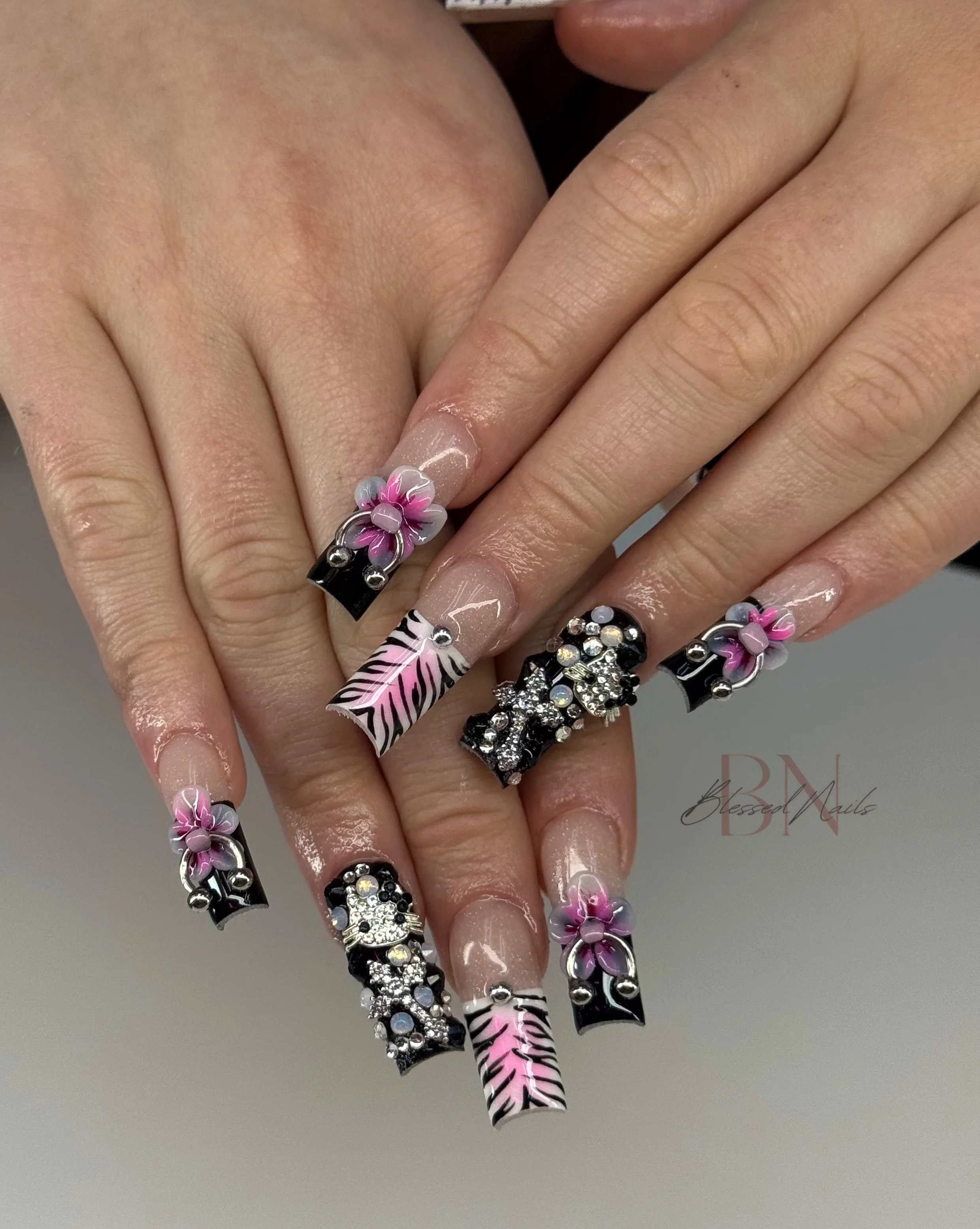 Close-up of hands with decorated nails featuring floral, zebra, and rhinestone designs.