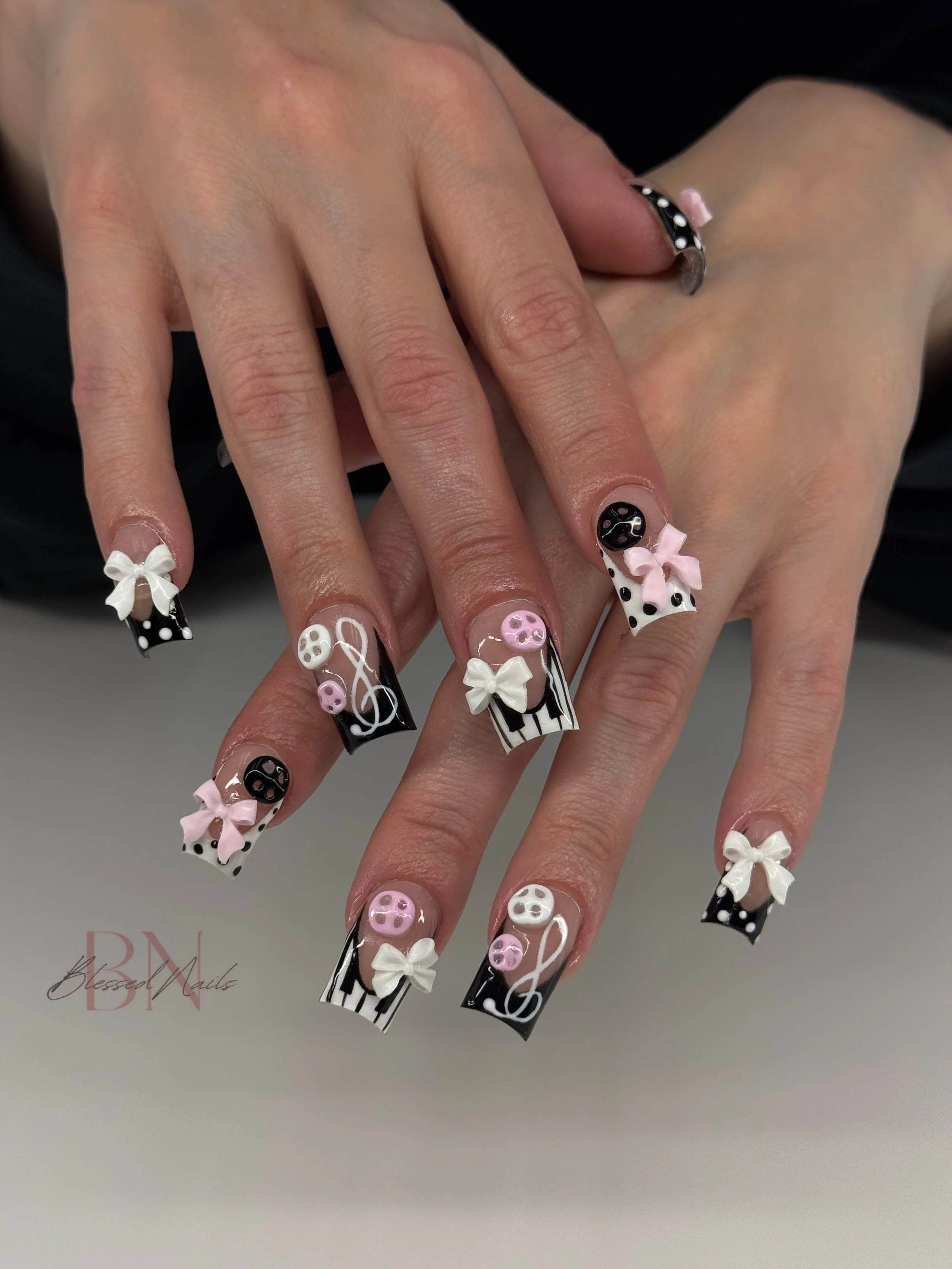 Nail art with black and white striped and polka dot patterns, pink bows, musical notes, and buttons on long square nails.