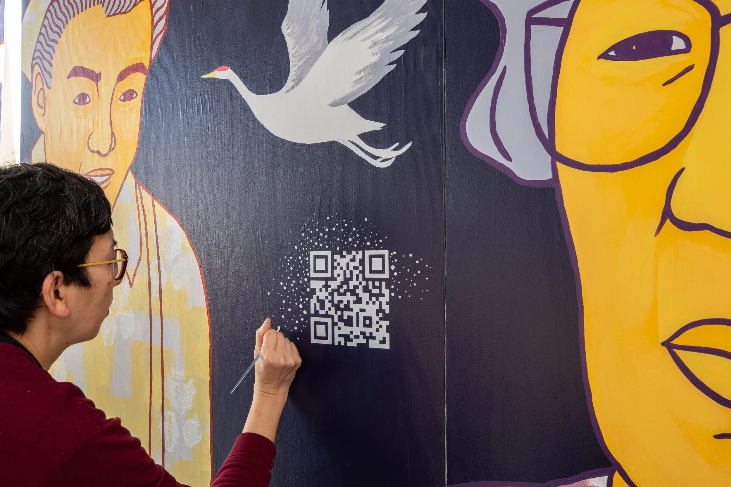 Michelle Kumata paints wite dots around a QR code on a mural to blend it with the artwork