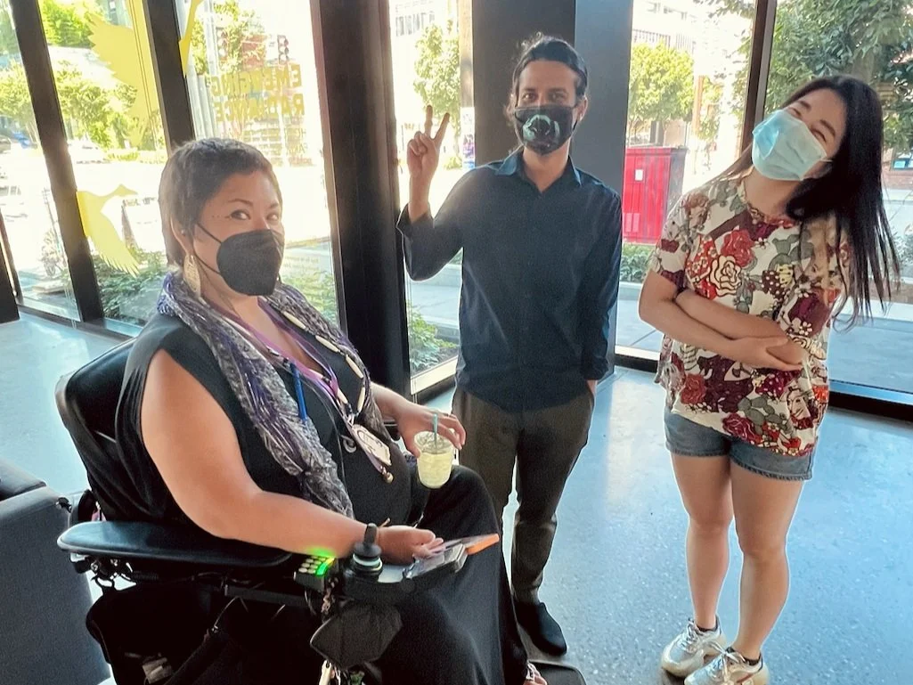 a person in a wheelchair and two others posing happily in a gallery