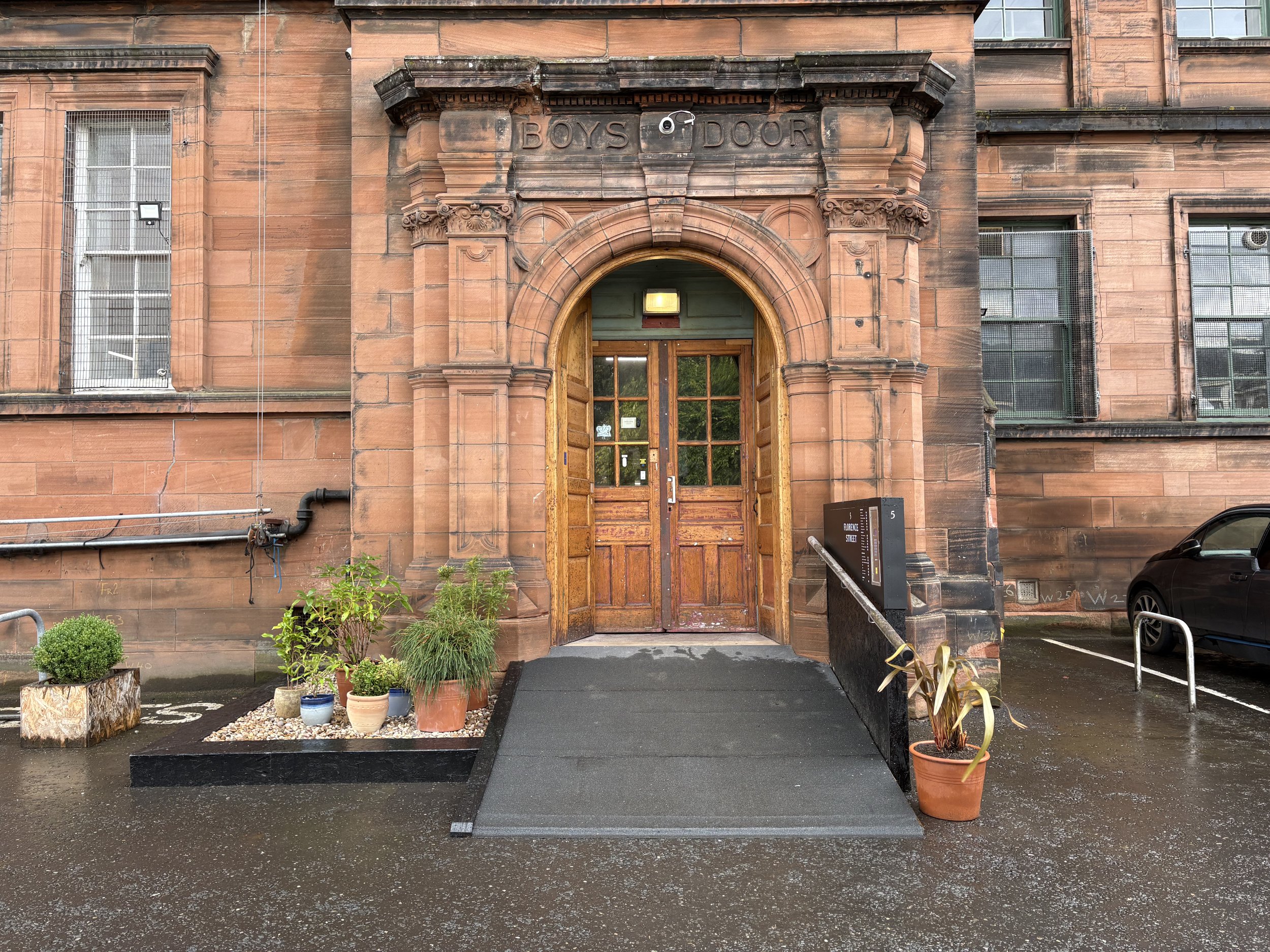 ramp leads up to the entrance of 5 Florence Street; a former school building built from red sandstone which has an ornate arched entrance way.