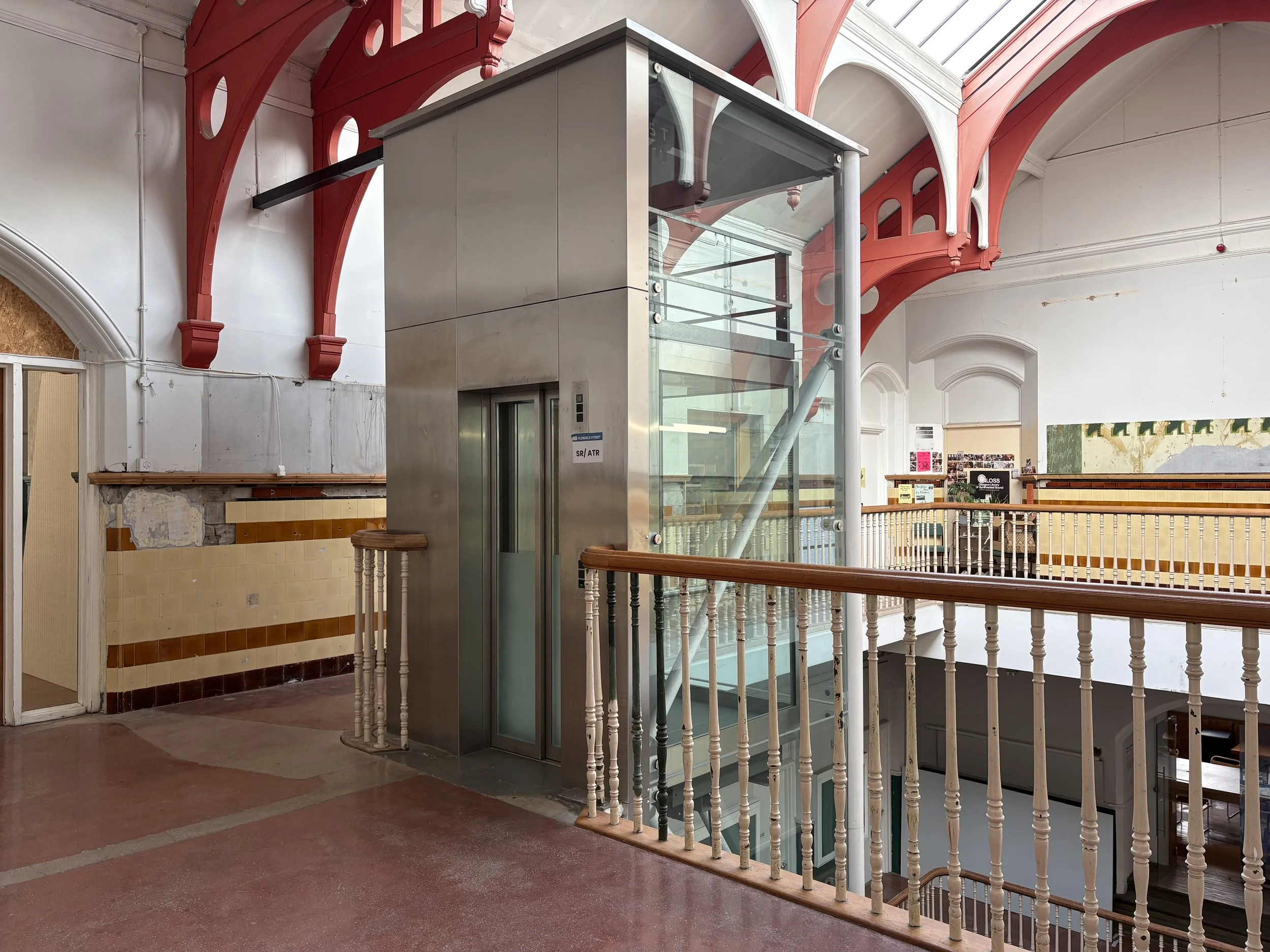 The top floor of an atrium with a large ornate skylight. A steel and glass lift descends through the central light well.