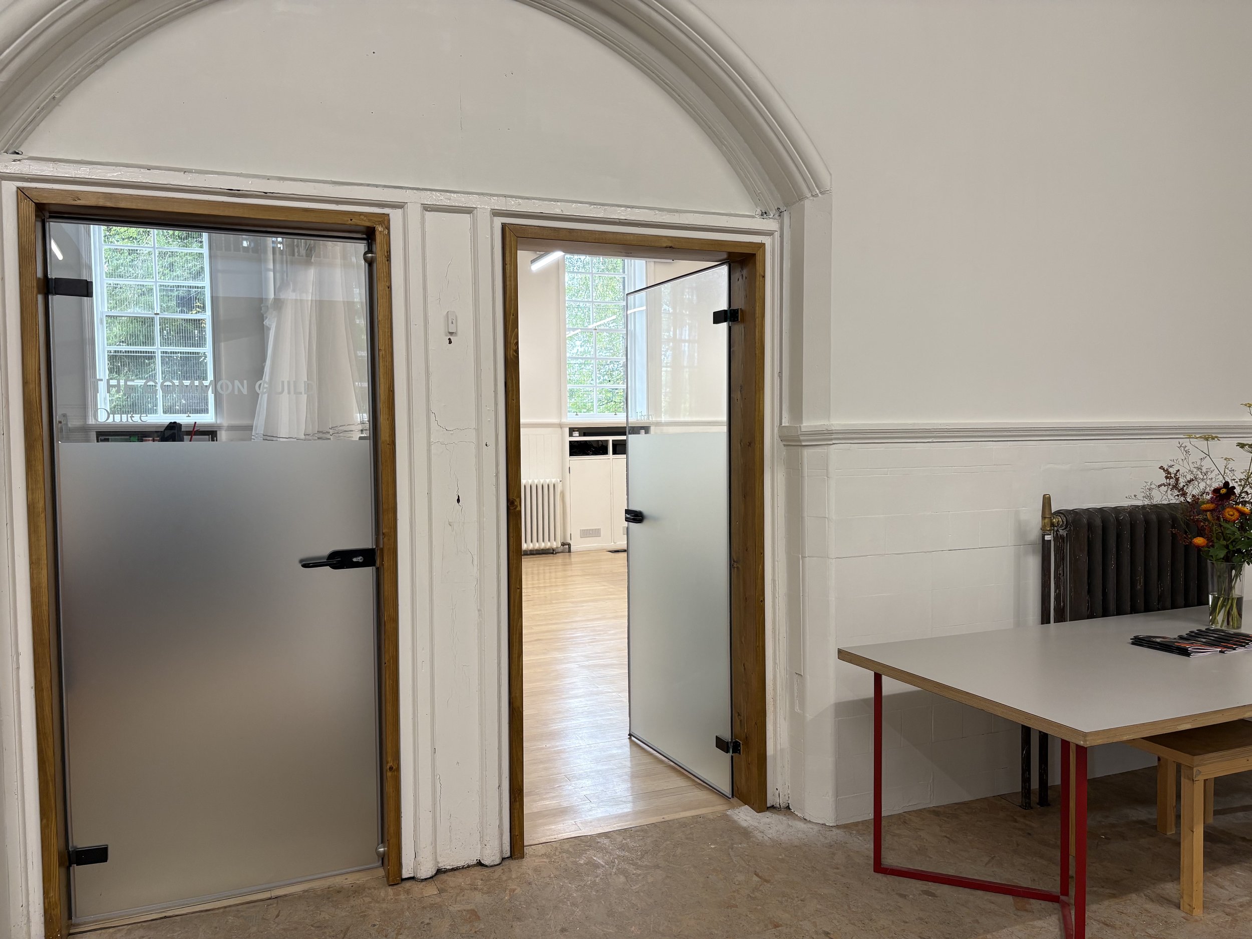 Two glass doors with partial opaque finishes. he door on the left is closed while the door on right is open and leads to a warmly lit room.