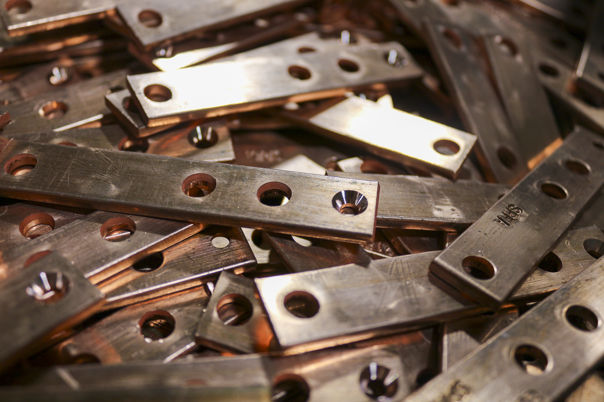 A pile of metallic machine parts with multiple holes, some with a shiny finish and others with a rusty appearance.