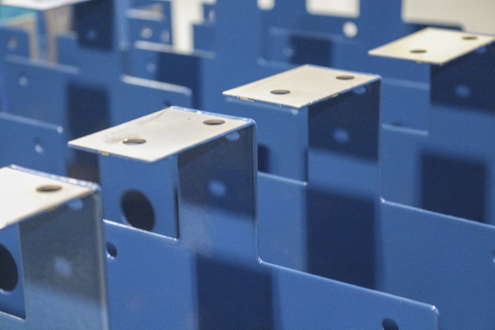 Multiple blue metal brackets or clips arranged in rows, some with holes on top