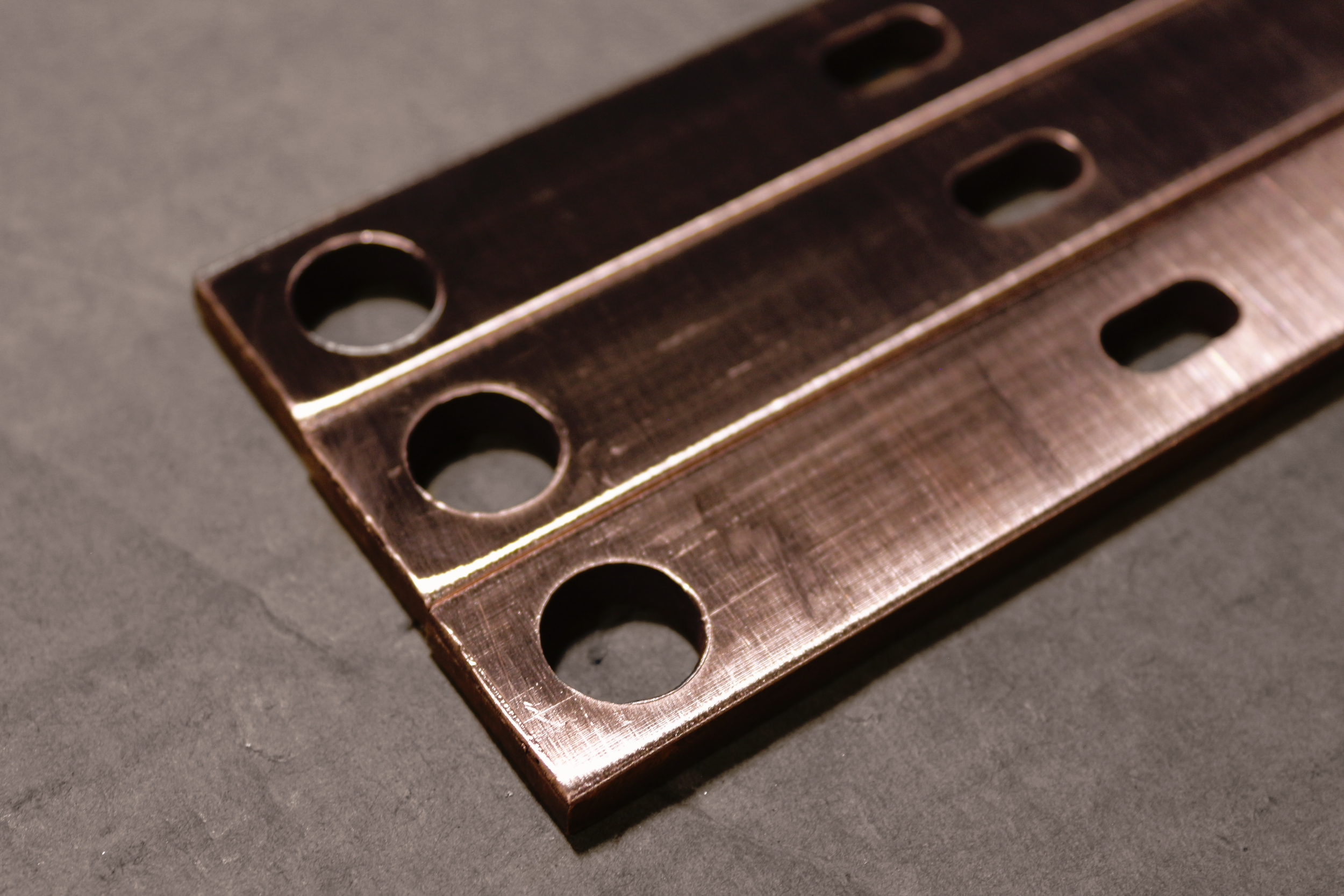 Multiple Small stamped copper components with two differing holes punched through the metal.
