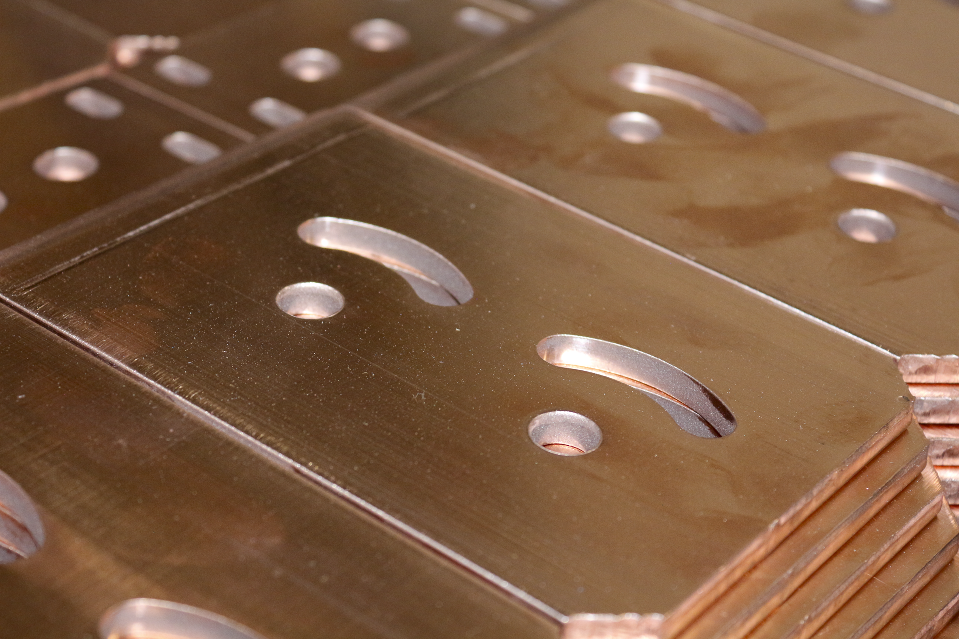 A stack of copper sheets with oval and circular cutouts.