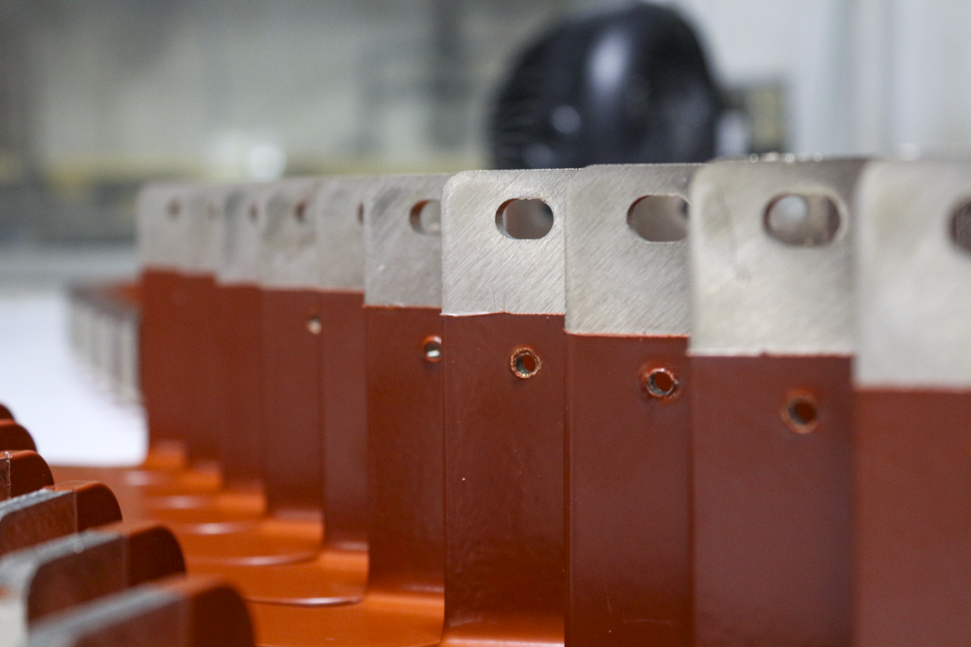 Close-up view of orange metal brake pads with silver metal attachment points in an industrial or manufacturing setting.