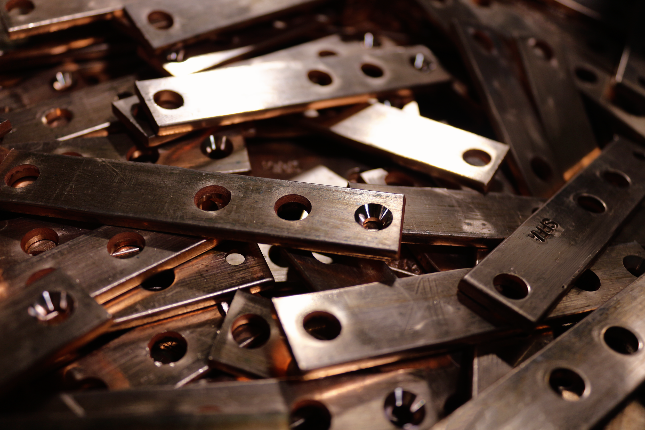 Multiple small copper components with stamped holes and machined/beveled hole edges.
