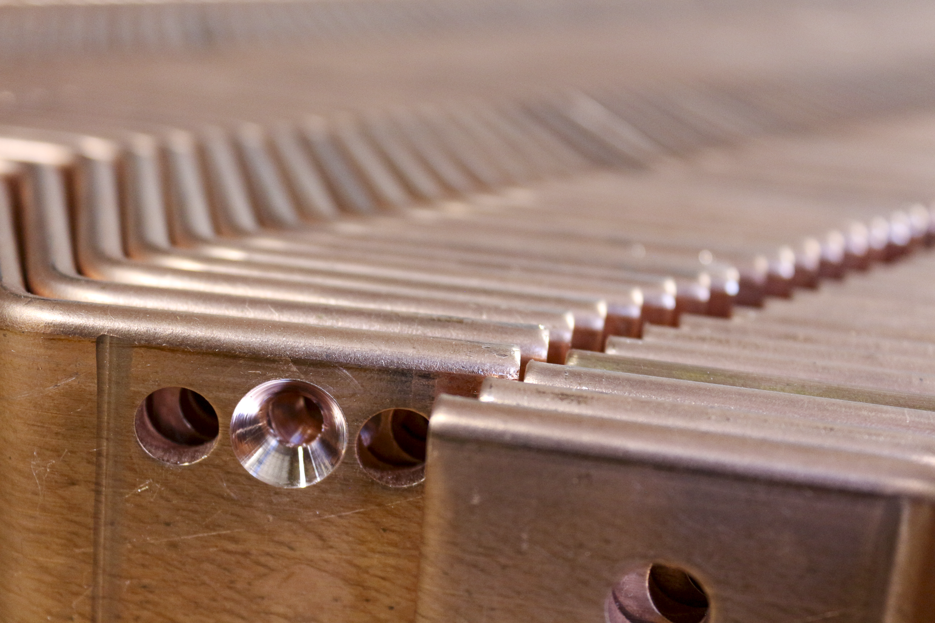 Close-up of a copper heat pipe with multiple holes and a shiny, flat surface.