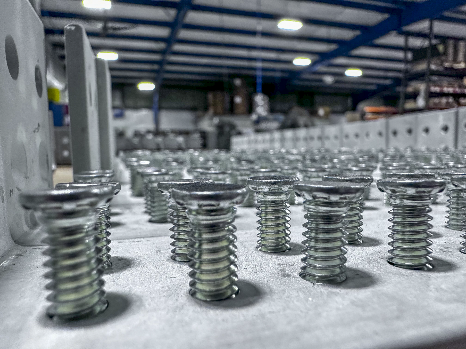 Close-up view of metal screws lined up on a surface in an industrial warehouse.