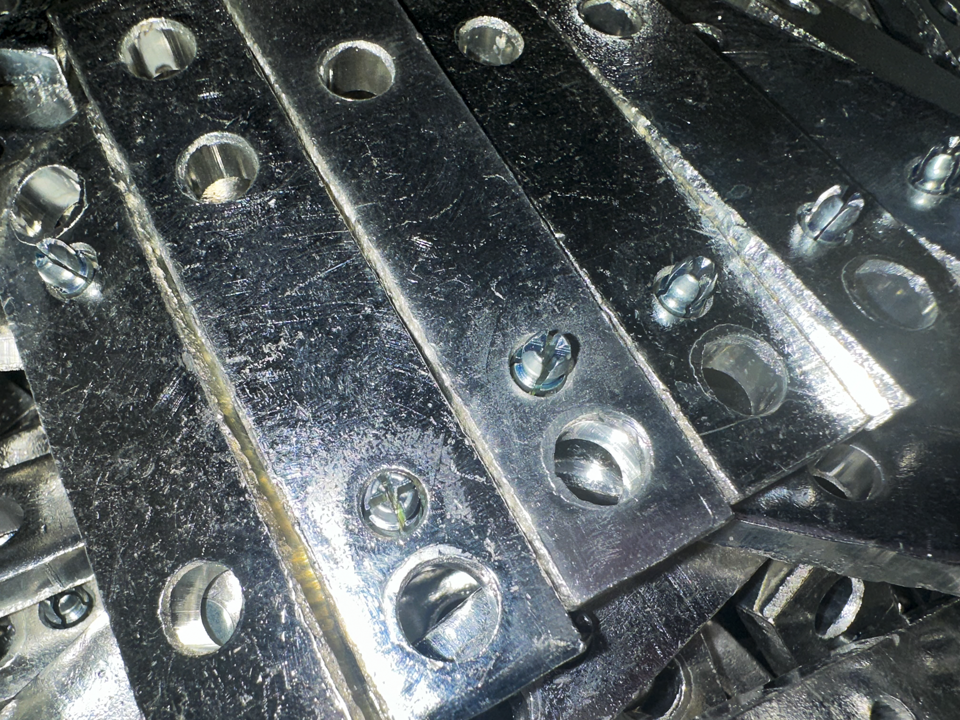Close-up of metallic engine components with drilled holes and screws, shiny and reflective surface.