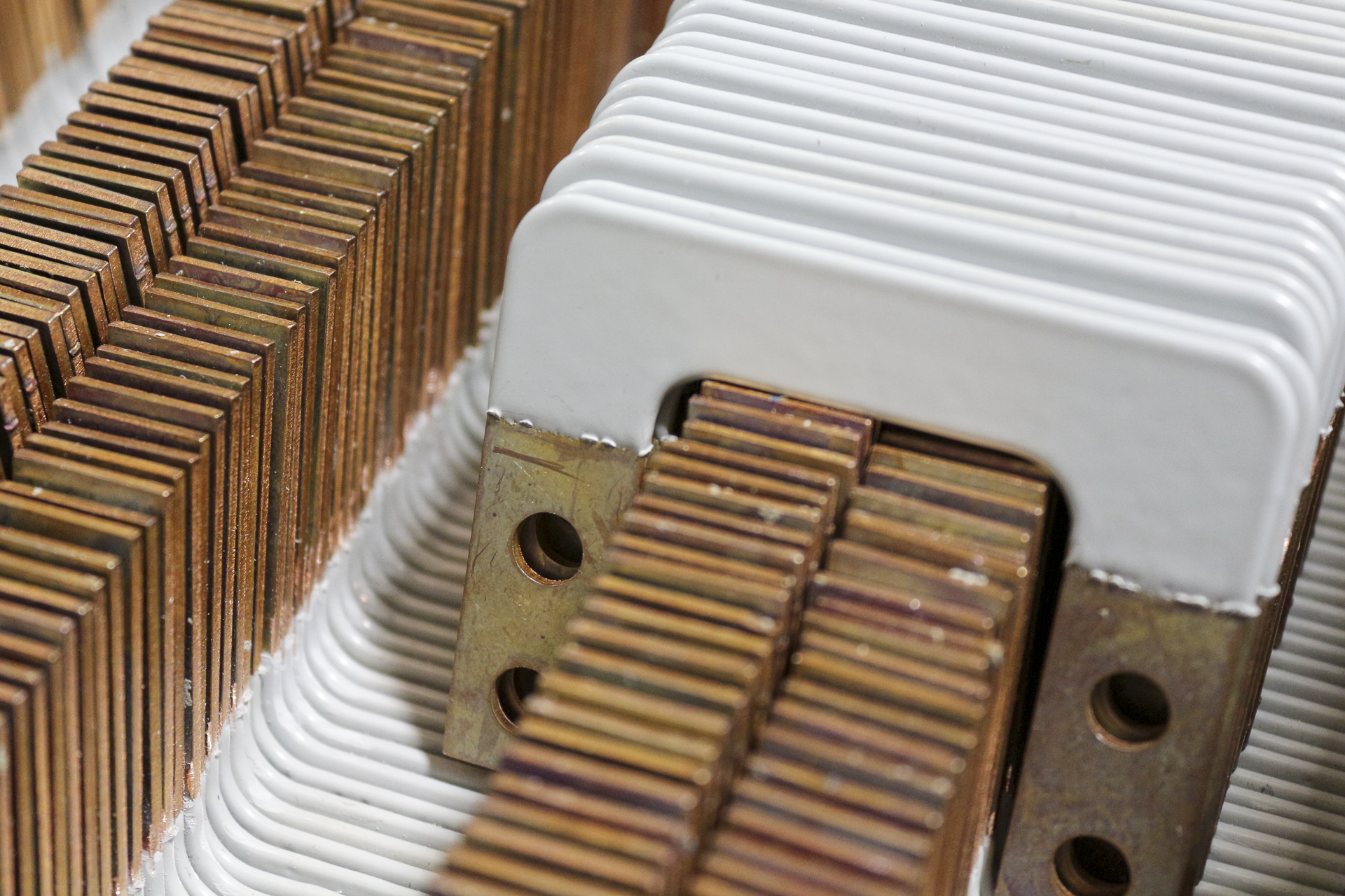 Close-up of electric transformer components, showing copper plates, white ceramic insulators, and metal mounting parts.