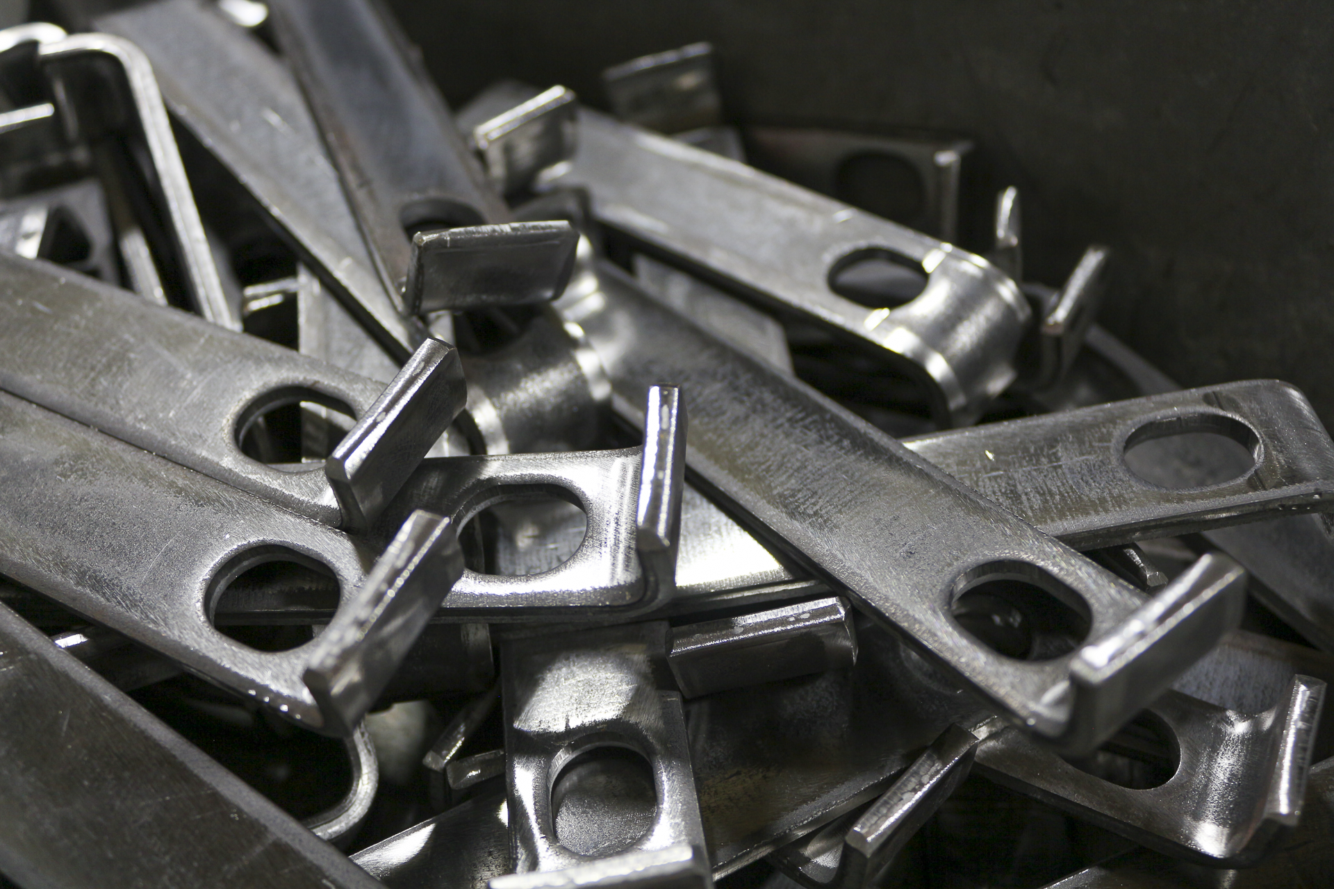 A pile of shiny, metallic metal parts with rectangular shapes and circular holes, overlapping each other.