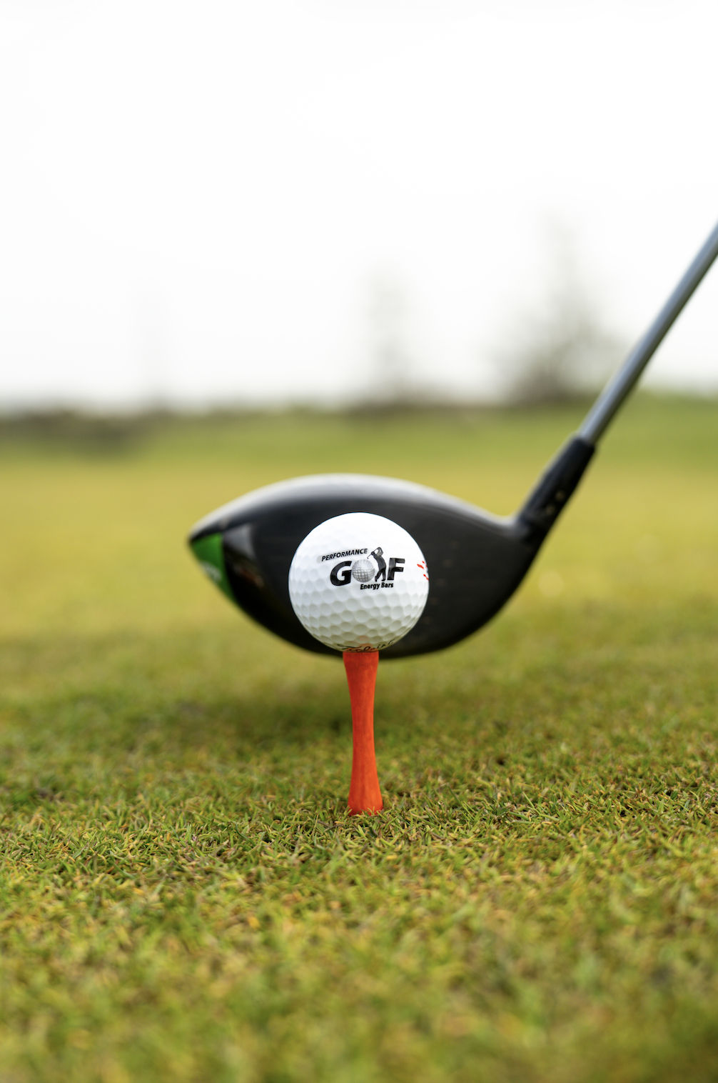 Close-up of a golf ball placed on a teed on a golf course, with a driver club positioned behind it and slightly out of focus.