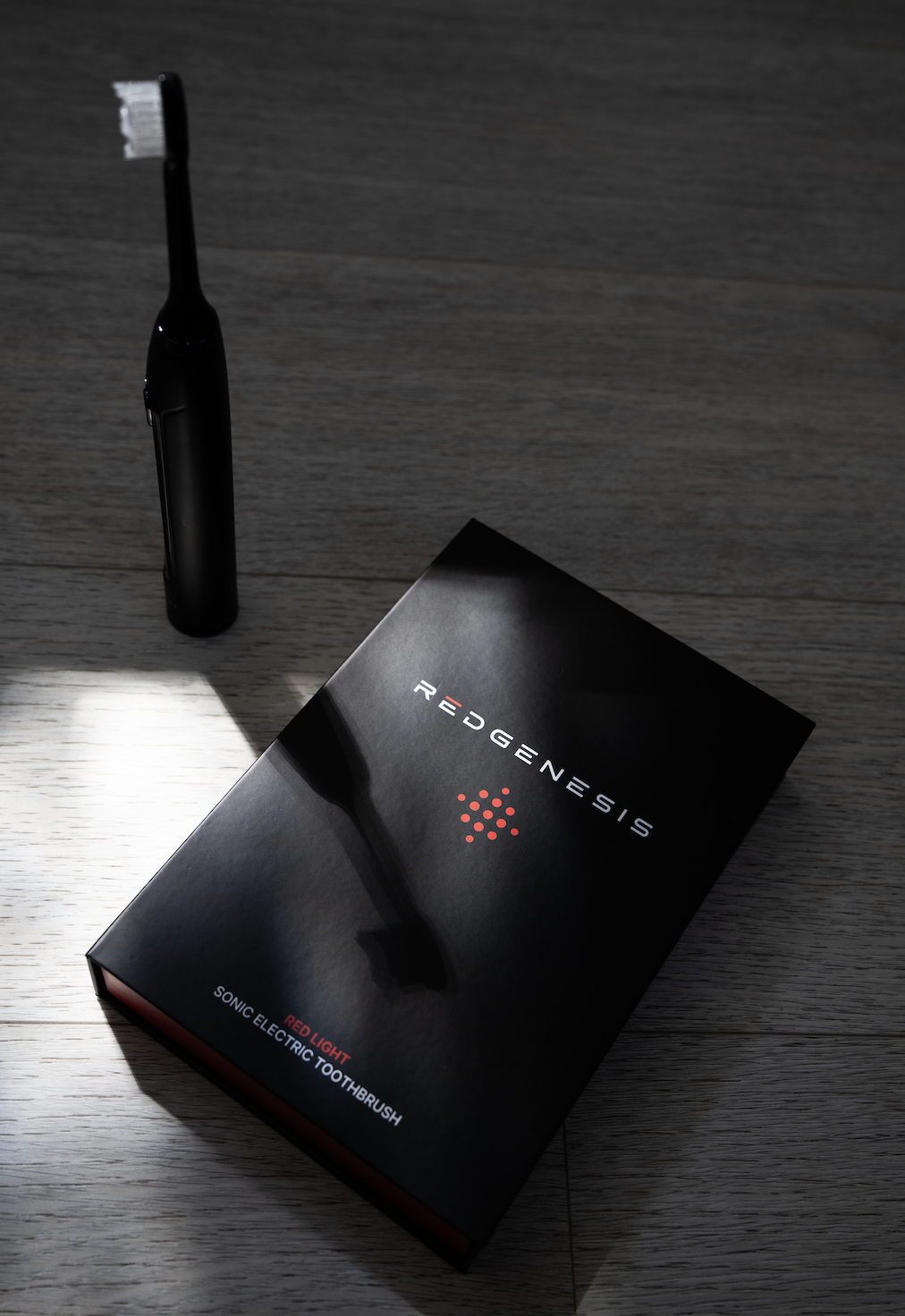 A black electric toothbrush standing upright next to a black box labeled 'Redeganesis Sonic Electric Toothbrush' on a wooden floor.