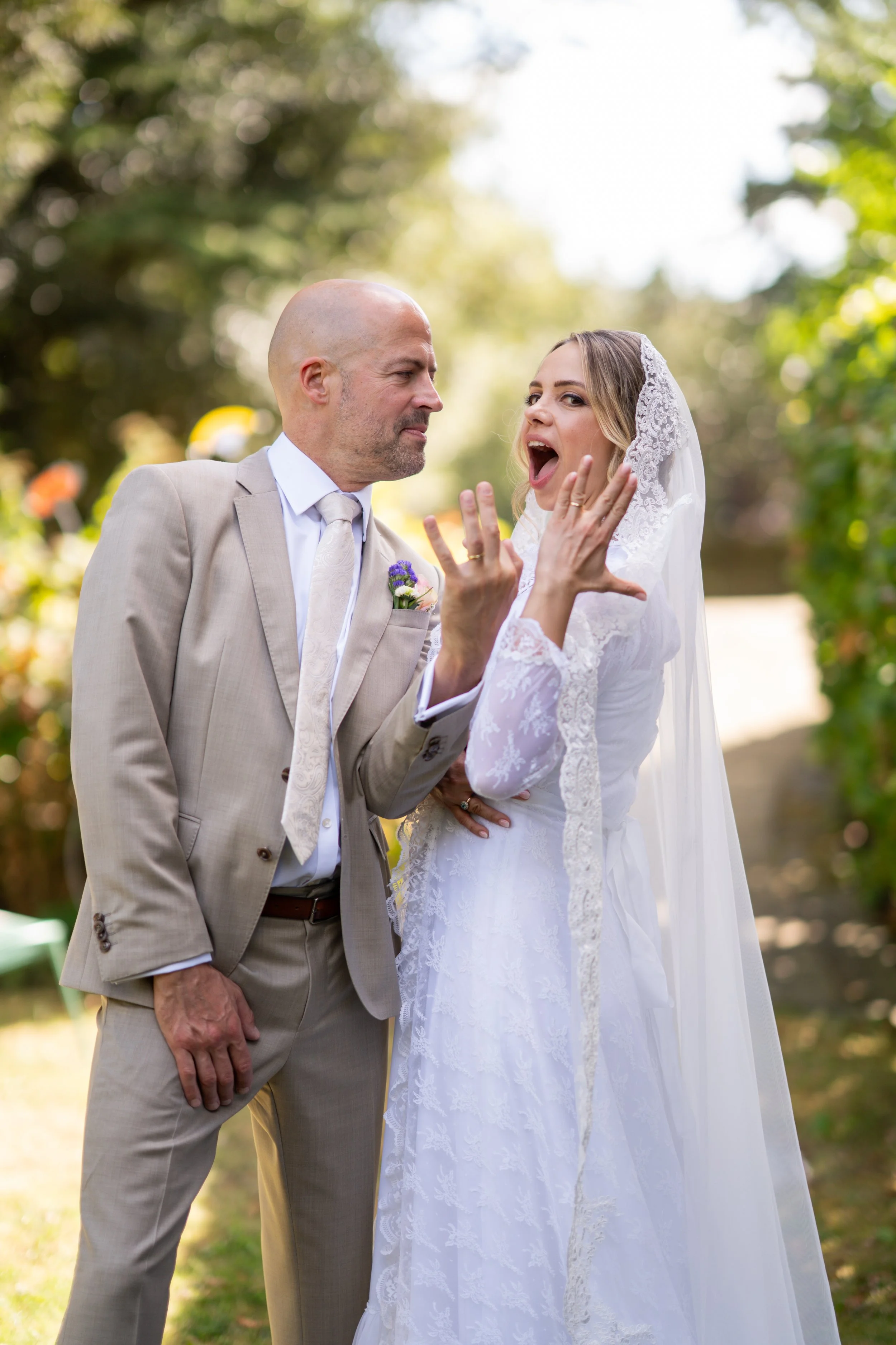 A bride and an older man in a beige suit are outdoors, with trees and sunlight in the background, during a wedding ceremony.