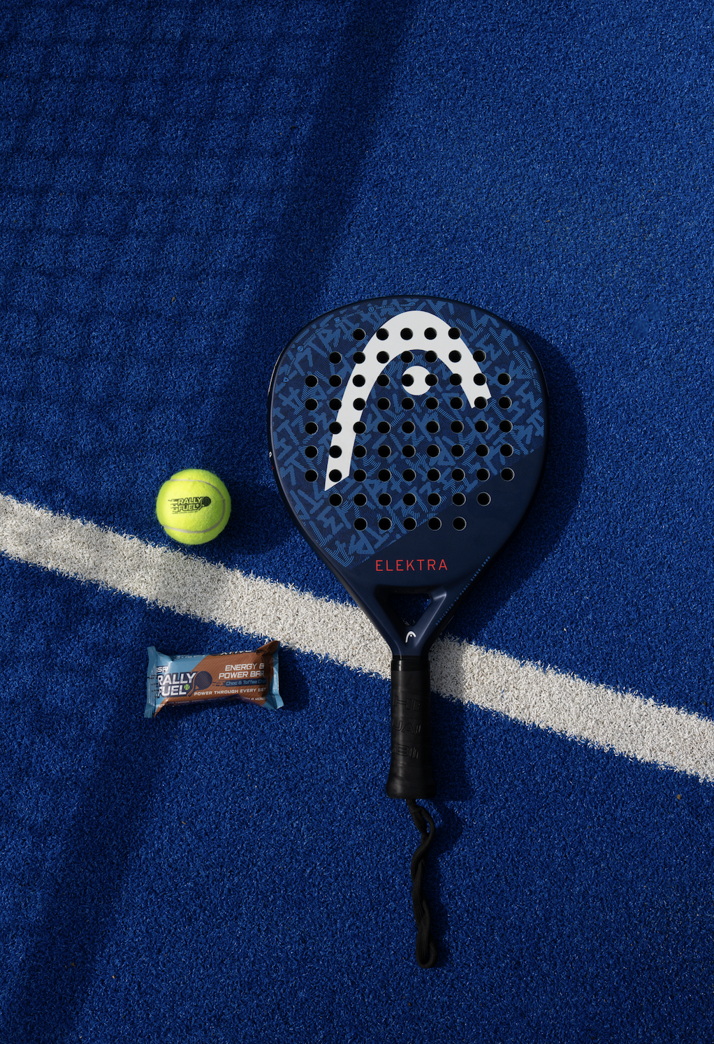 Padel racket, tennis ball, and energy bar on a blue sports court.