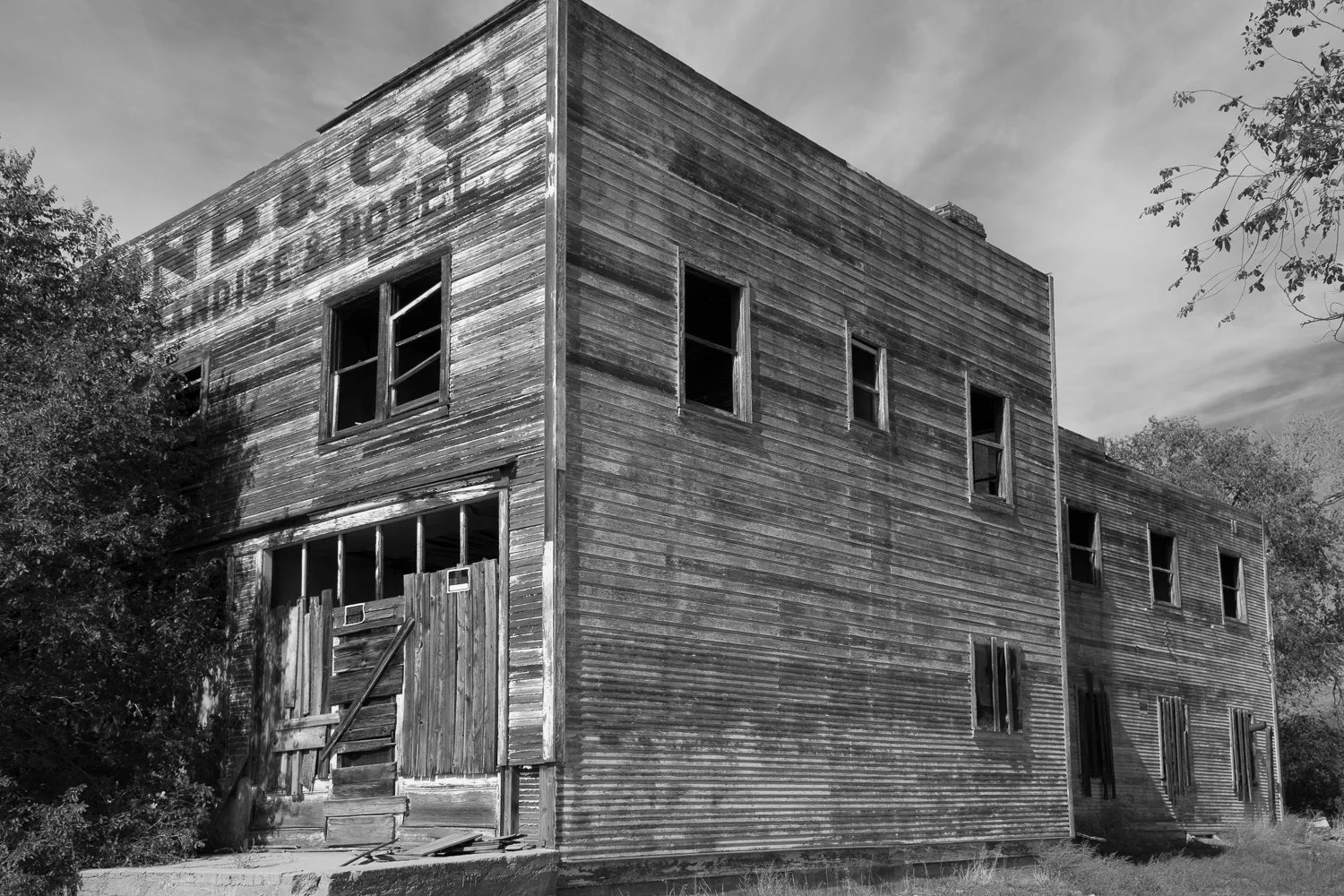 A weathered two-story wooden building with faded painted signage and boarded first-floor windows.