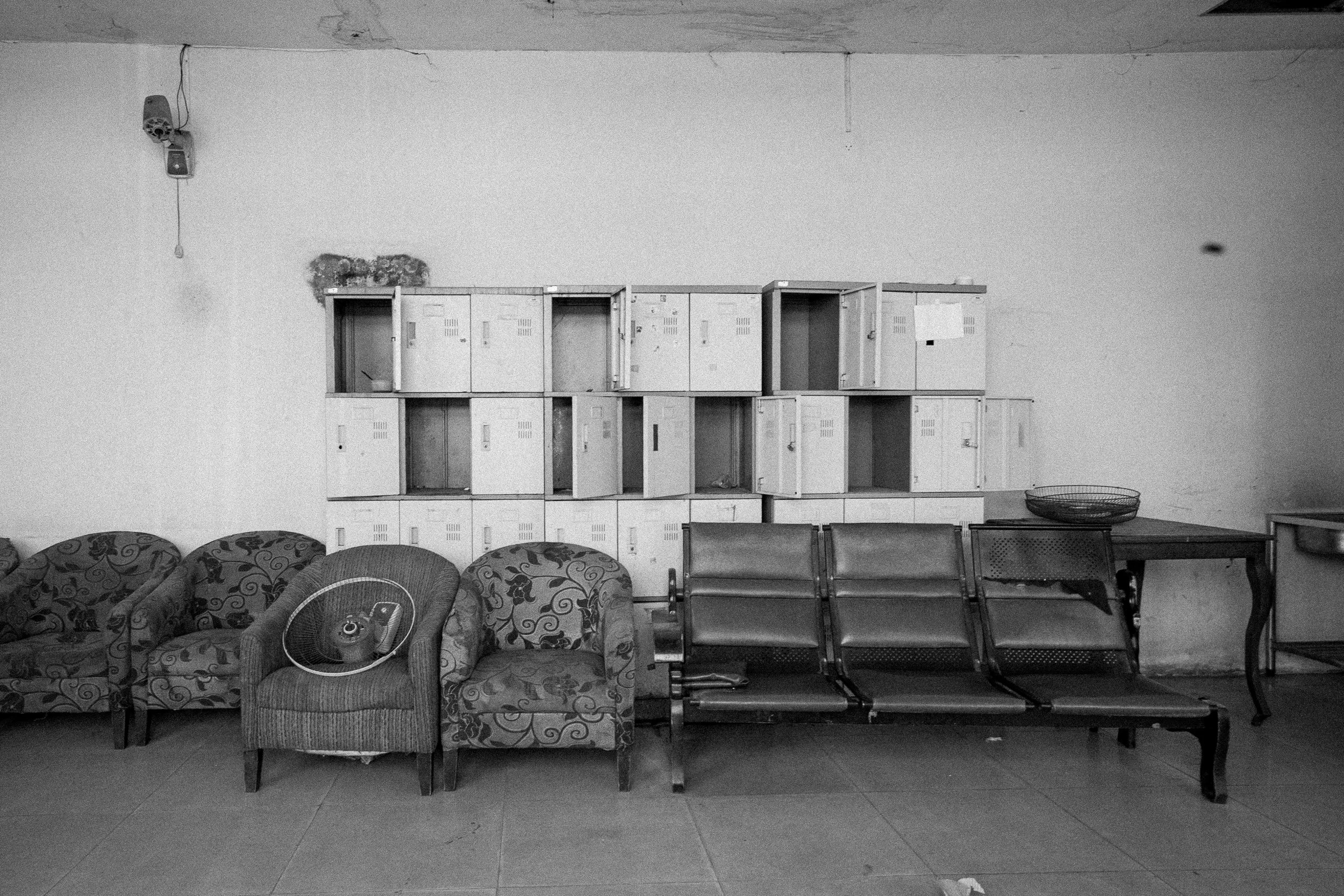 Abandoned upholstered armchairs and a metal bench beneath rows of open storage lockers.