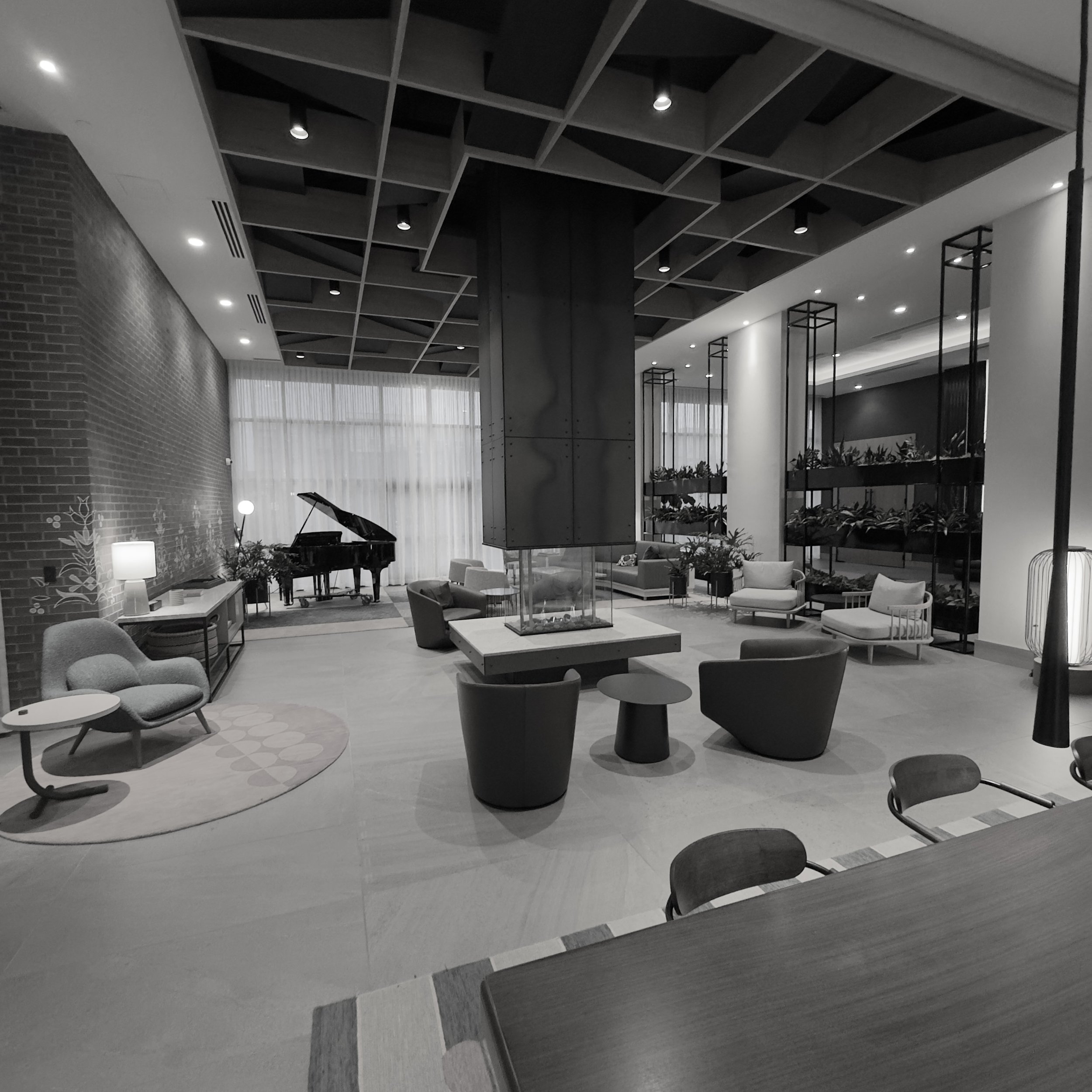 Modern lounge chairs and a grand piano in a spacious hotel lobby with a slatted ceiling.